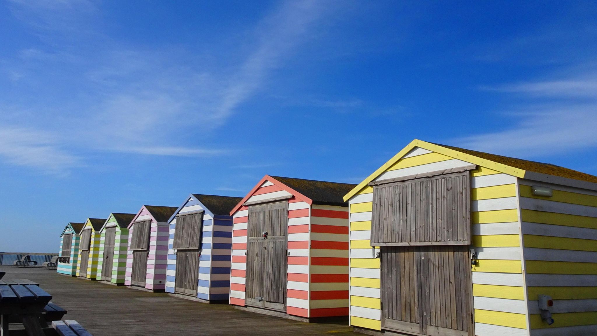 Hazy cloud in a blue sky above a row of seven beach huts along the coast in Hastings, East Sussex