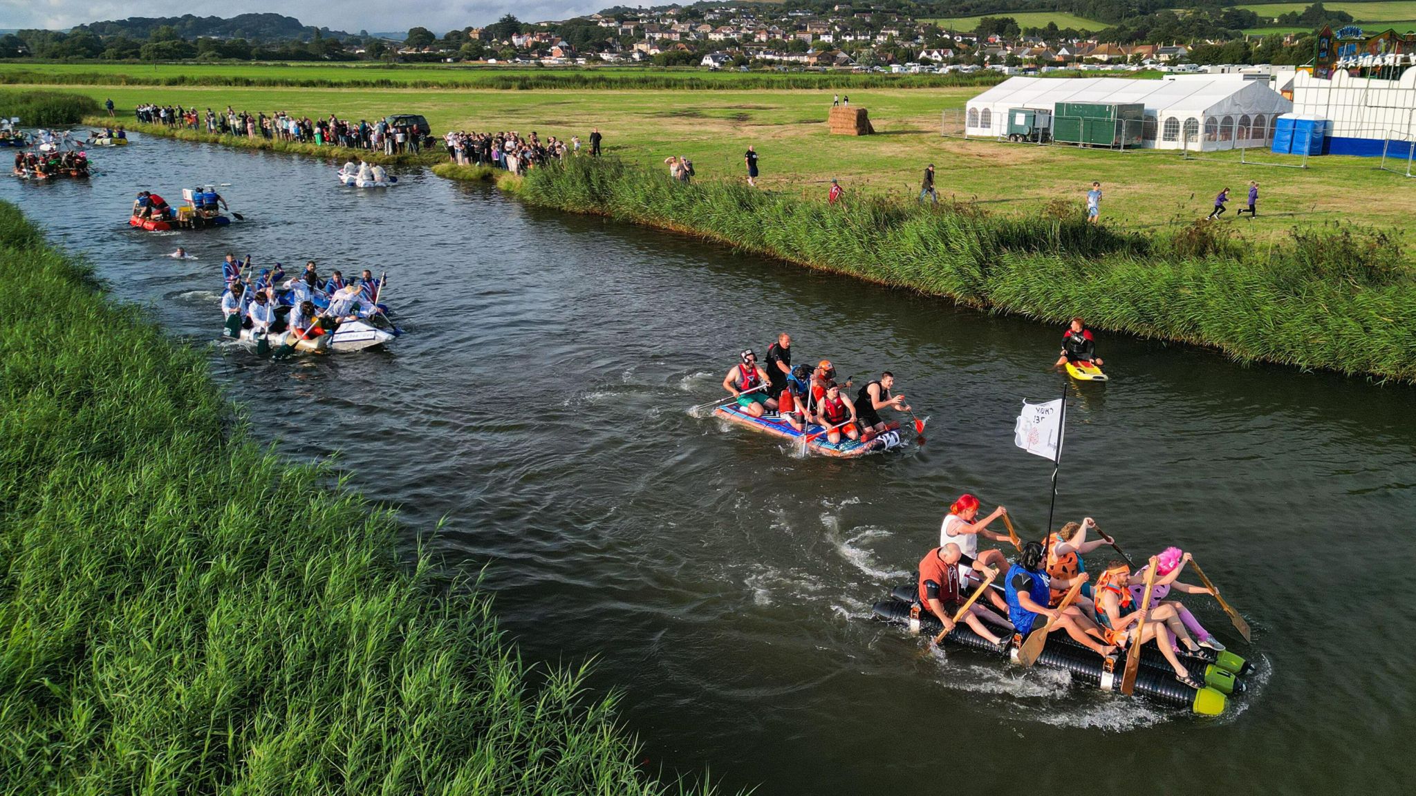 People in fancy dress and homemade rafts drifting down a river