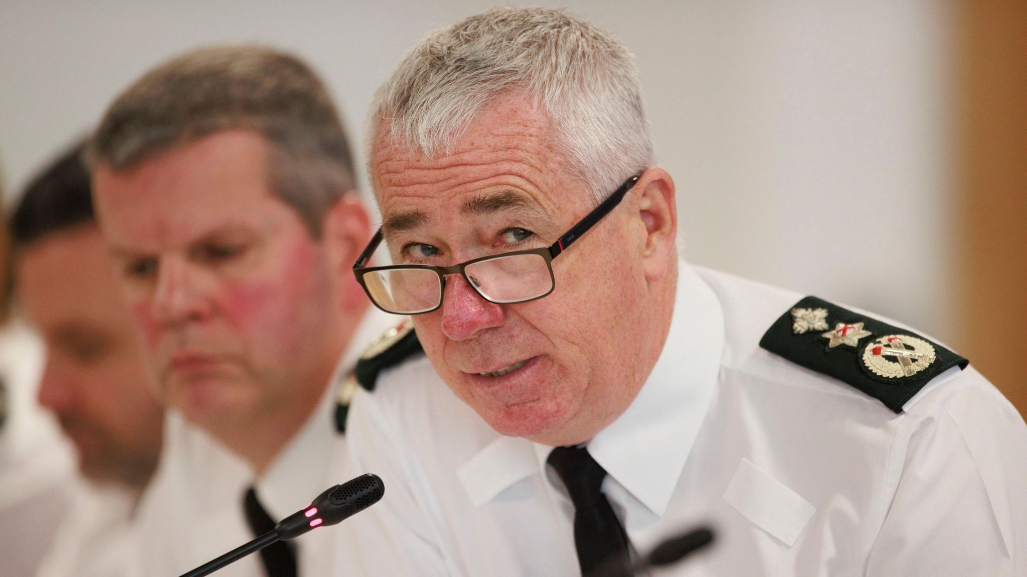 PSNI Chief Constable Jon Boutcher, in uniform, leans over a mic at a conference