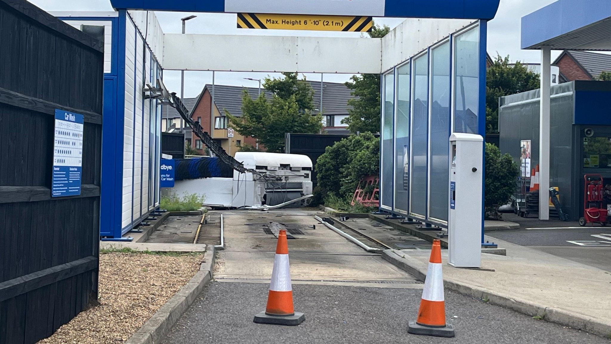 Two orange cones block the entrance to a car wash, which has glass panelling and a damaged piece of machinery at the back