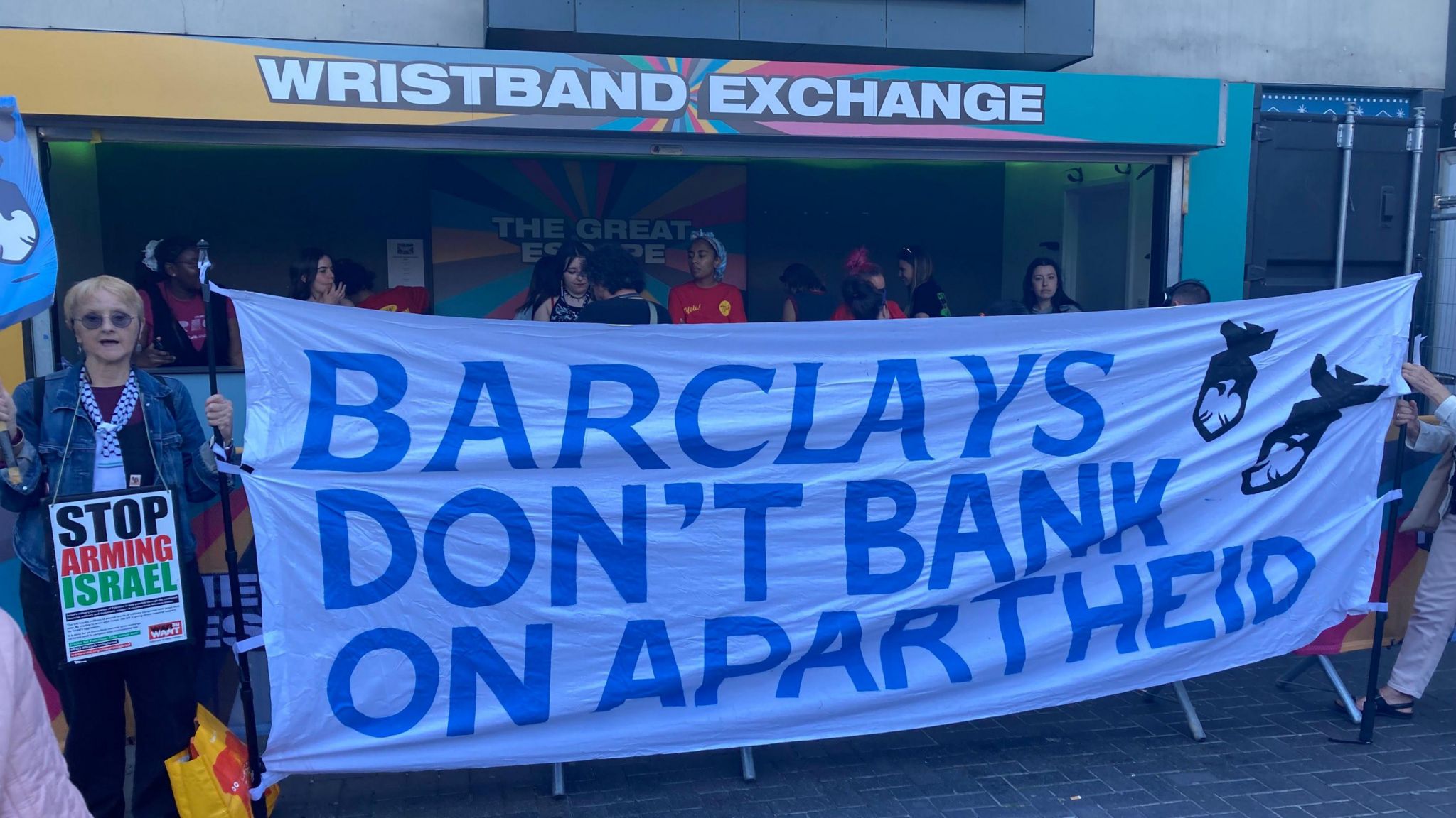 A banner reading "Barclays don't bank on apartheid" being held up outside a festival wristband exchange