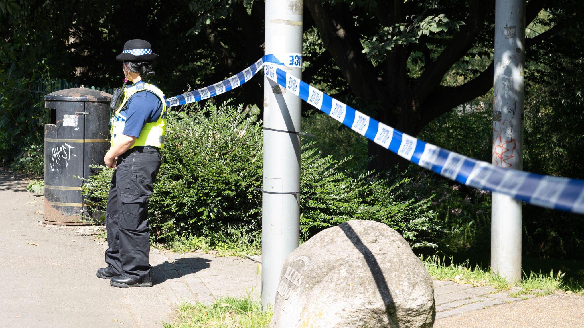 Police officer standing by police tape on edge of a park