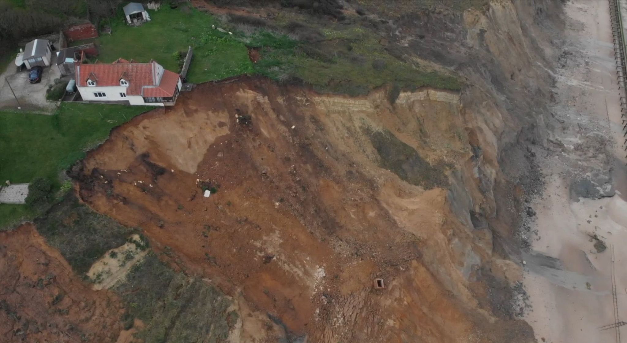 A drone image of the farmhouse partially hanging over the cliff edge