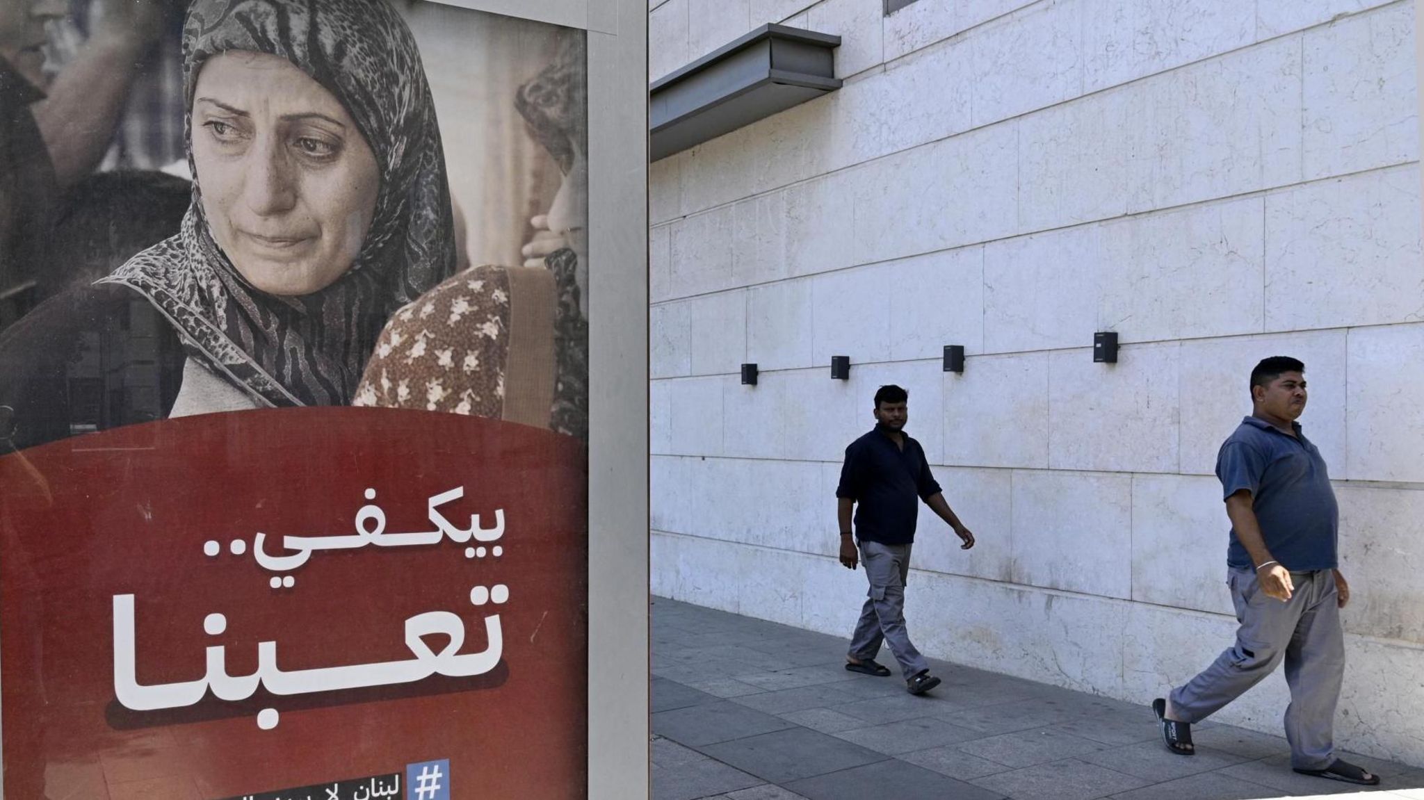 Men walk past a billboard in Beirut, Lebanon, with the caption "Enough, we are tired... Lebanon does not want war." (13 August 2024)