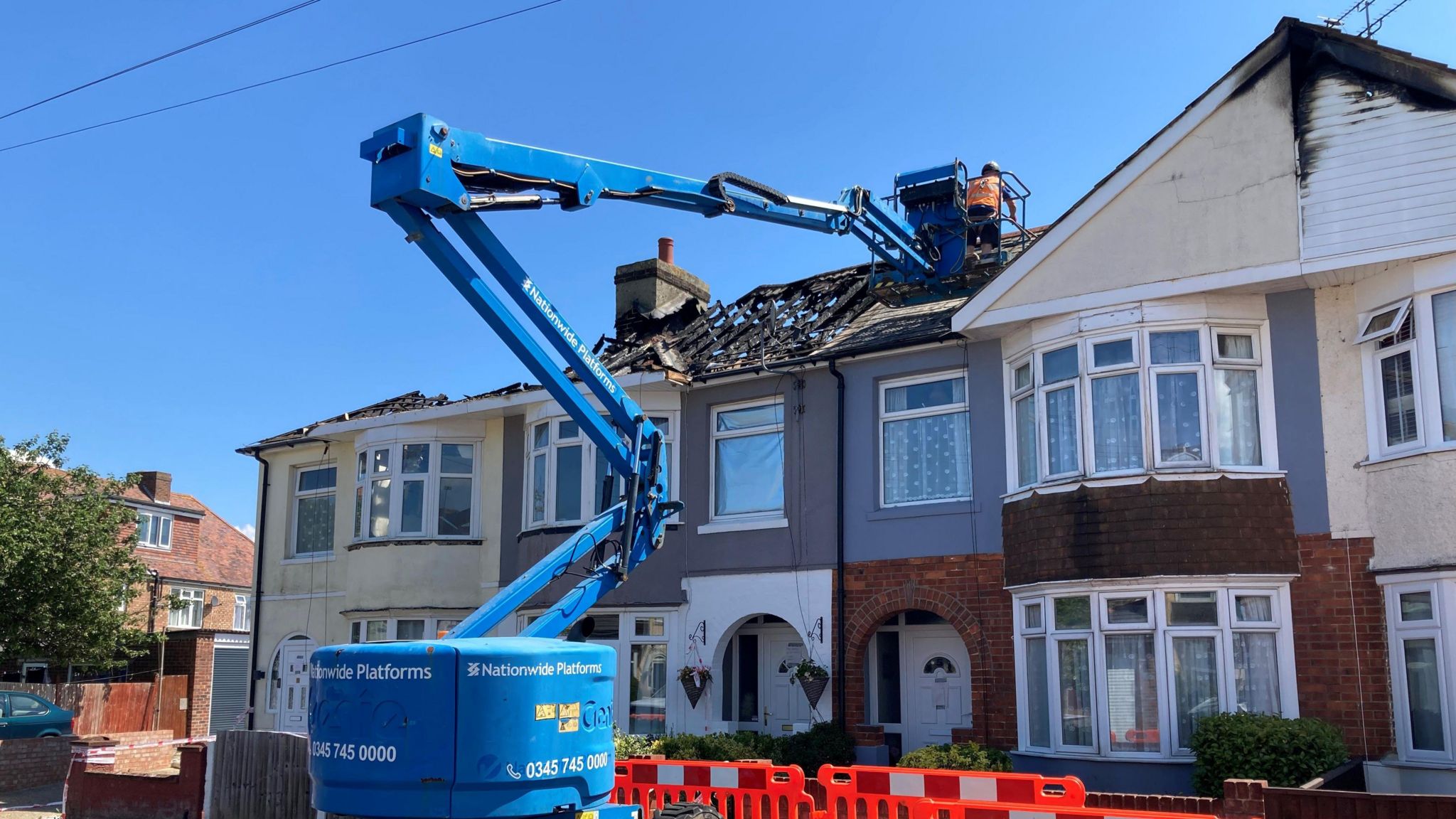 Workers on a blue crane dismantling a fire-damaged roof over a row of terraced houses