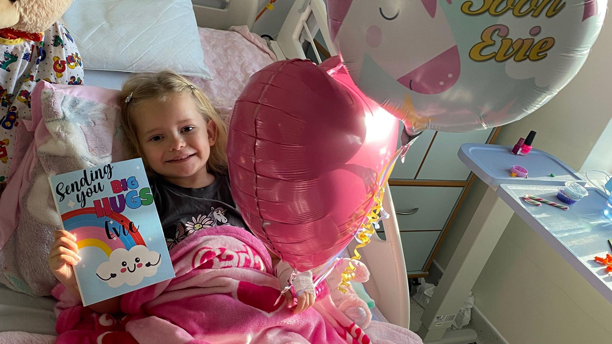 Girl in hospital bed with get well card and balloons