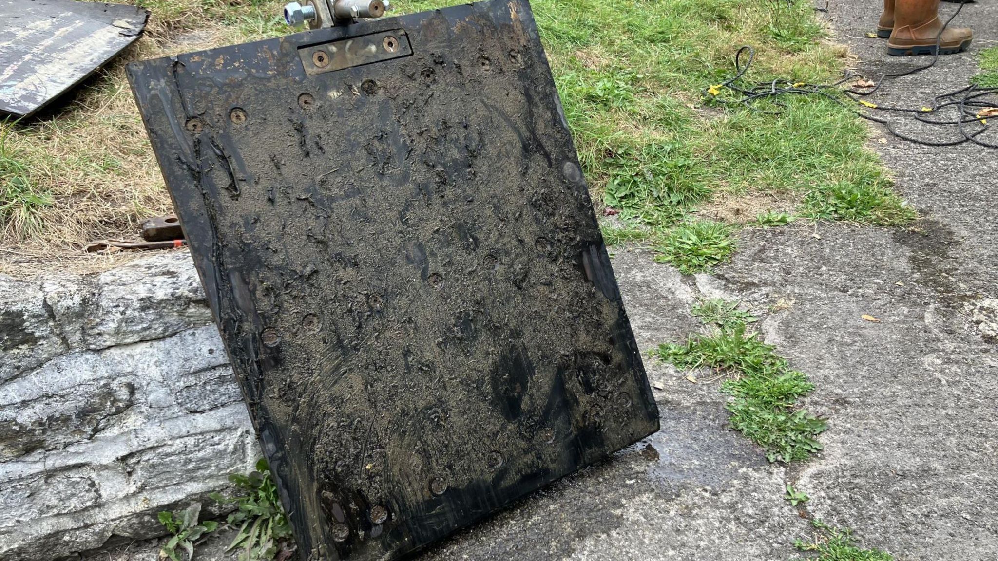 Black rectangular panel leant up against a low stone wall