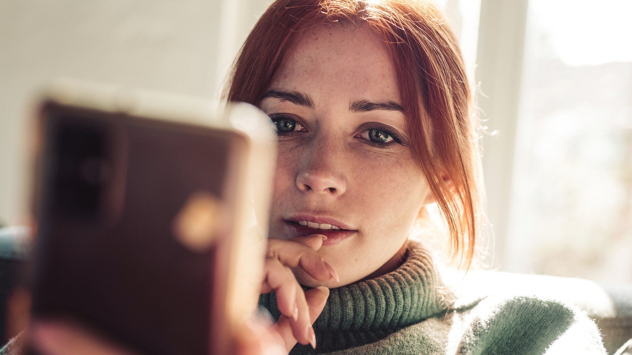 Woman with red hair looking on screen of her mobile phone