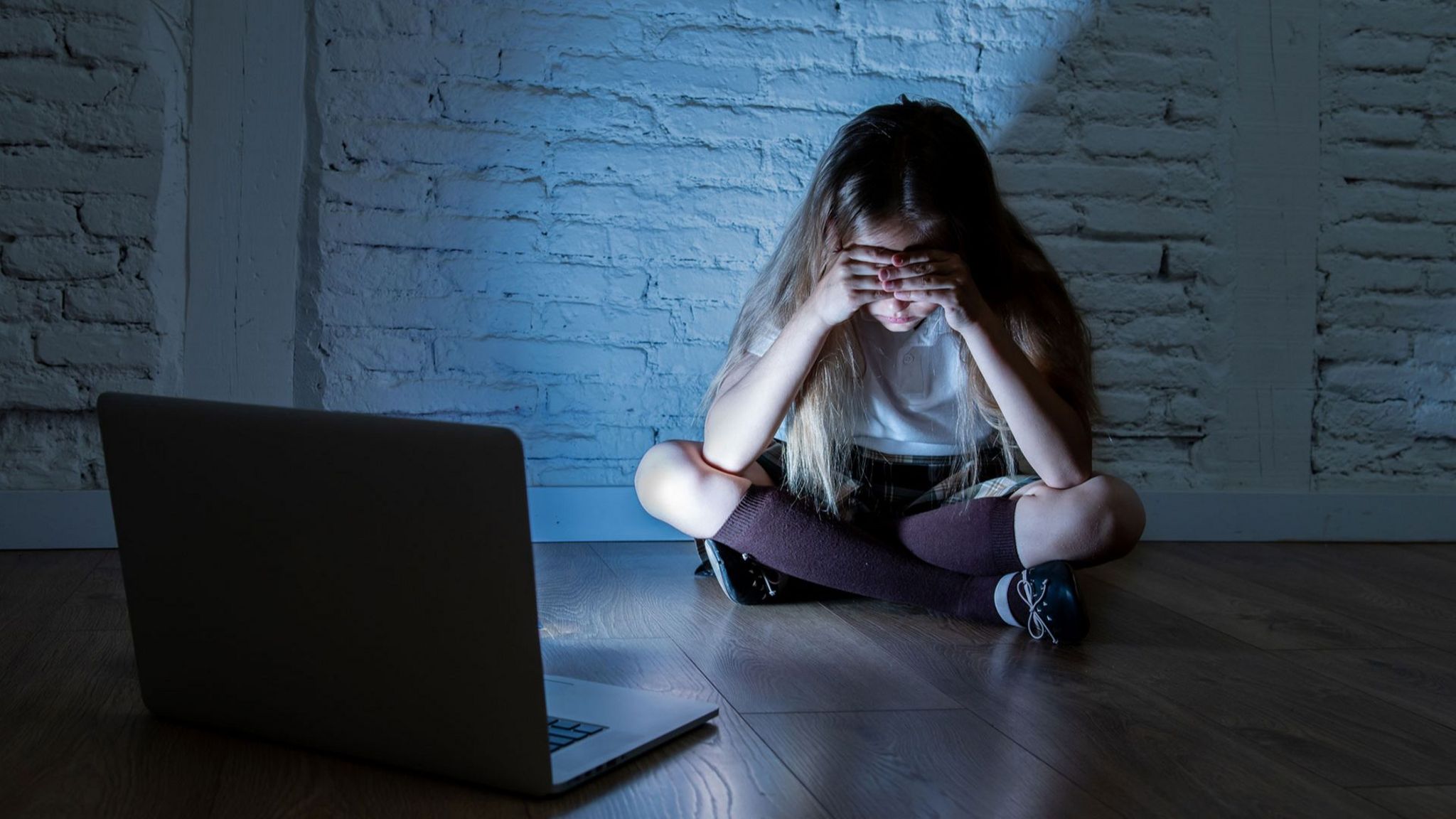 A girl buries her head in her hands in front of a laptop screen in an empty room in this stock image