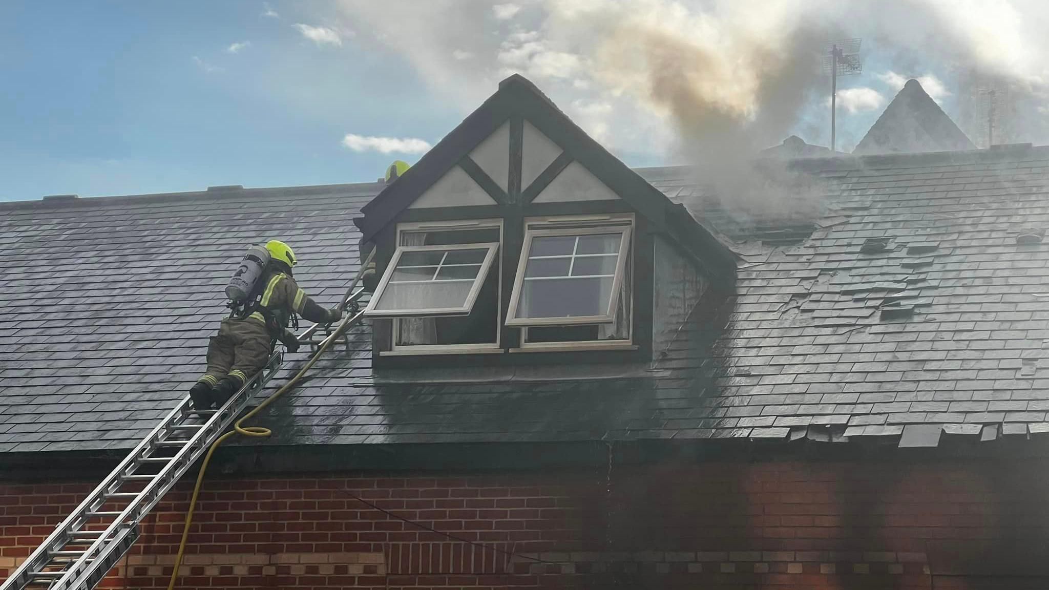 A firefighter on a ladder outside a window with smoke 