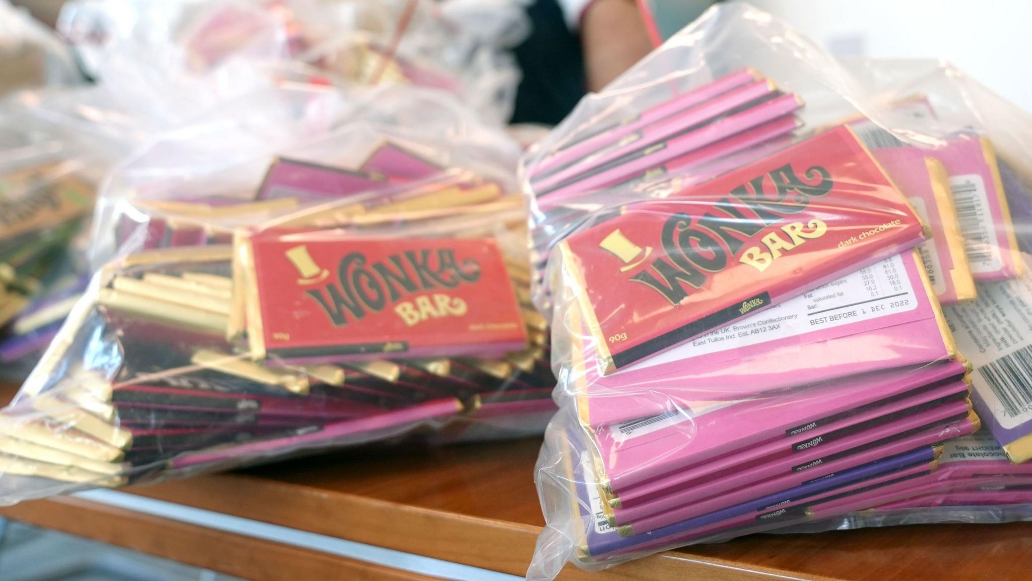 Large see-through plastic sacks containing Wonka chocolate bars in red and pink wrapping, on a table