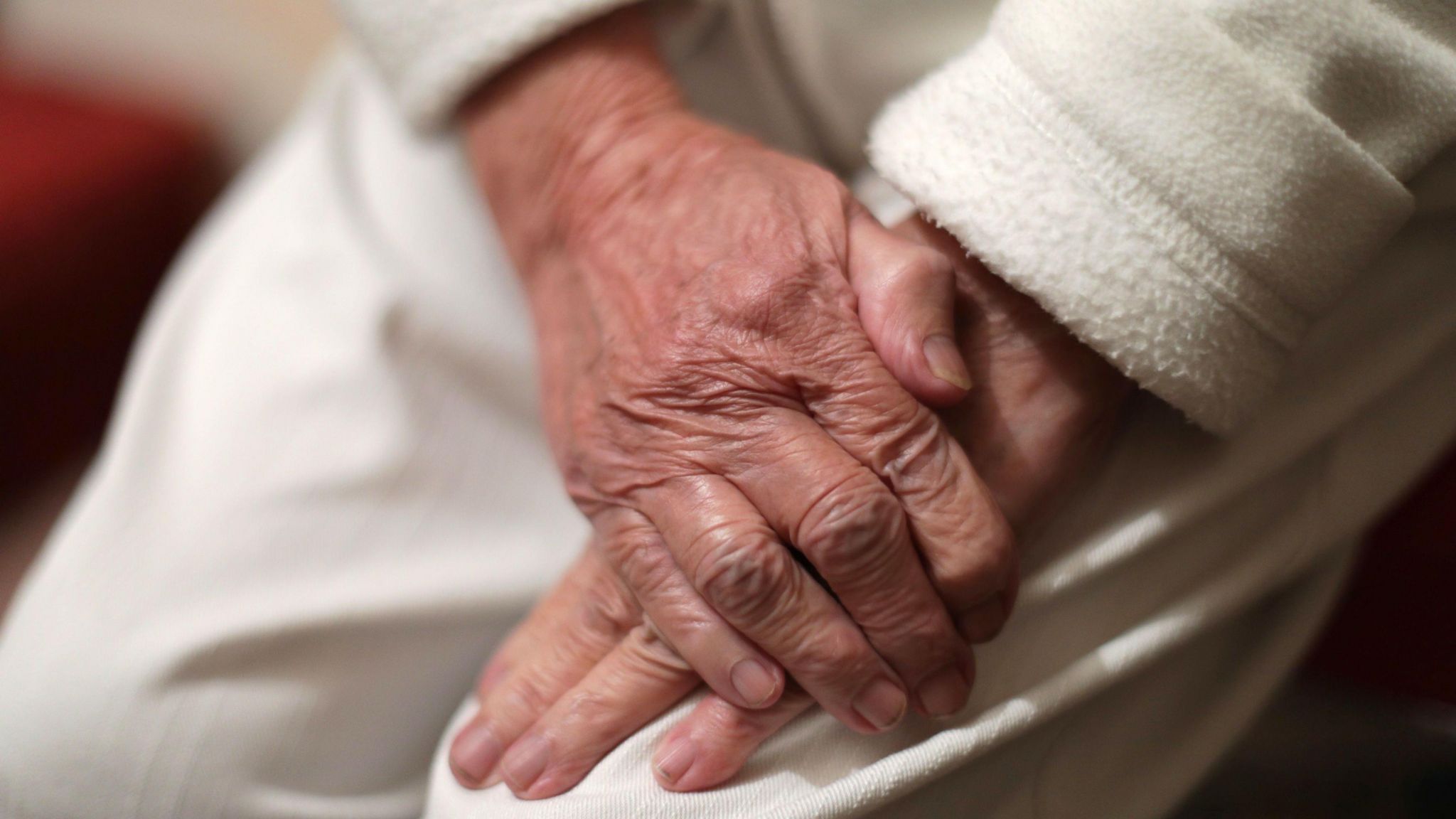 An elderly person rests their hands on their knee