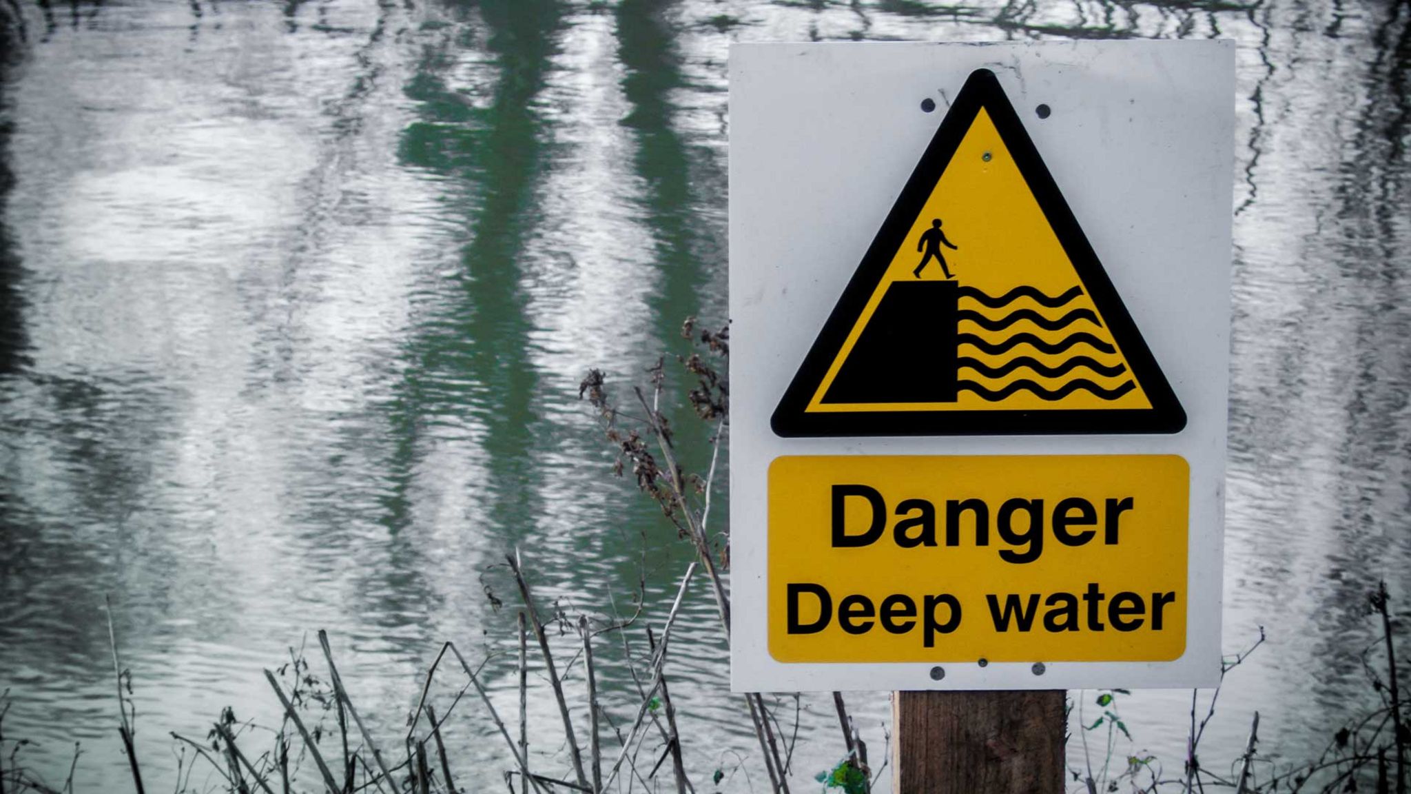Sign reading "Danger Deep Water" by a lake