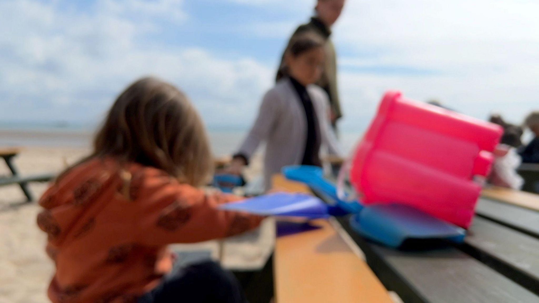 A blurred image of two children by a bench on a beach with their mother
