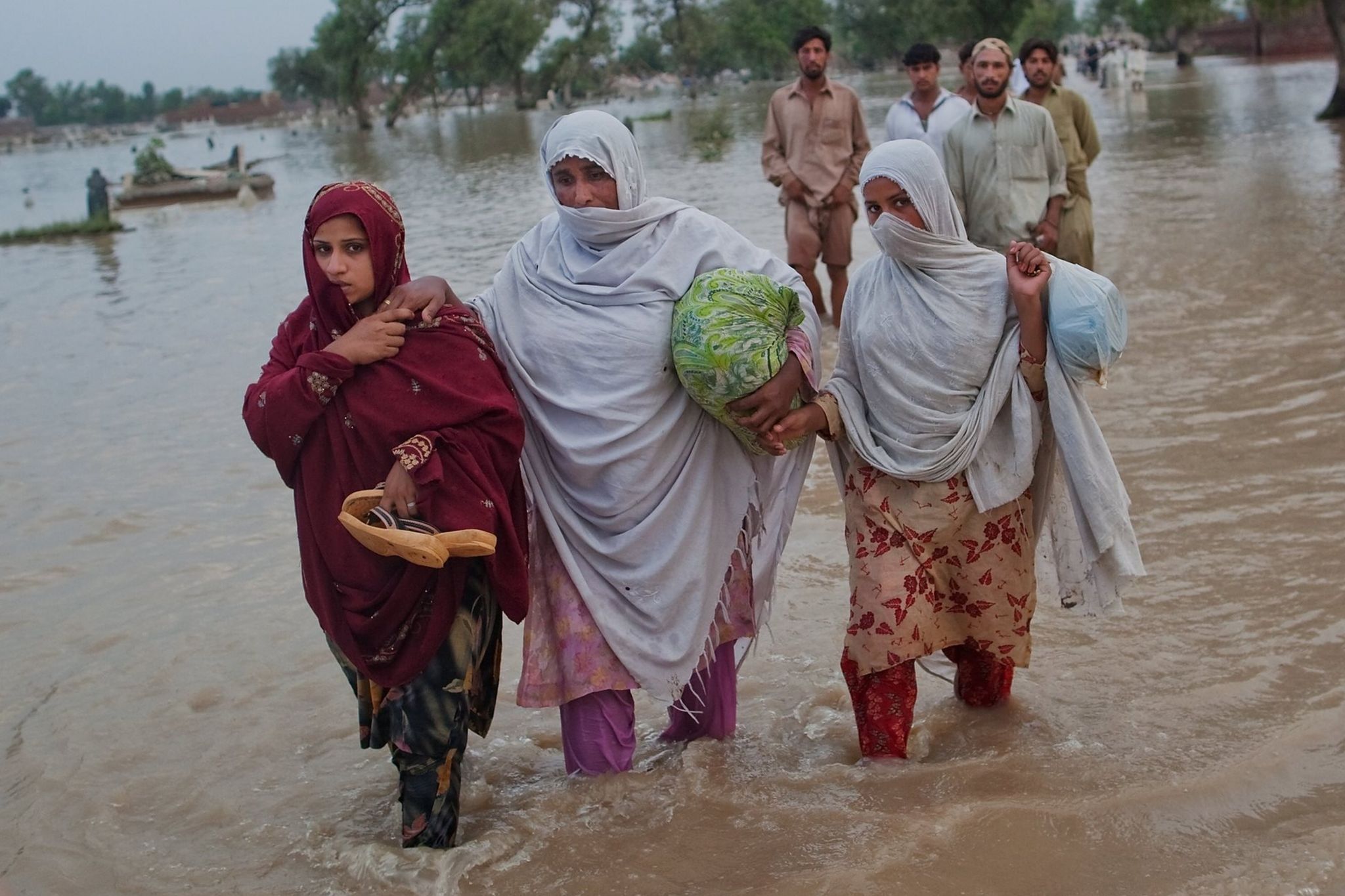 Three women in Pakistan wade through floodwater, carrying their belongings