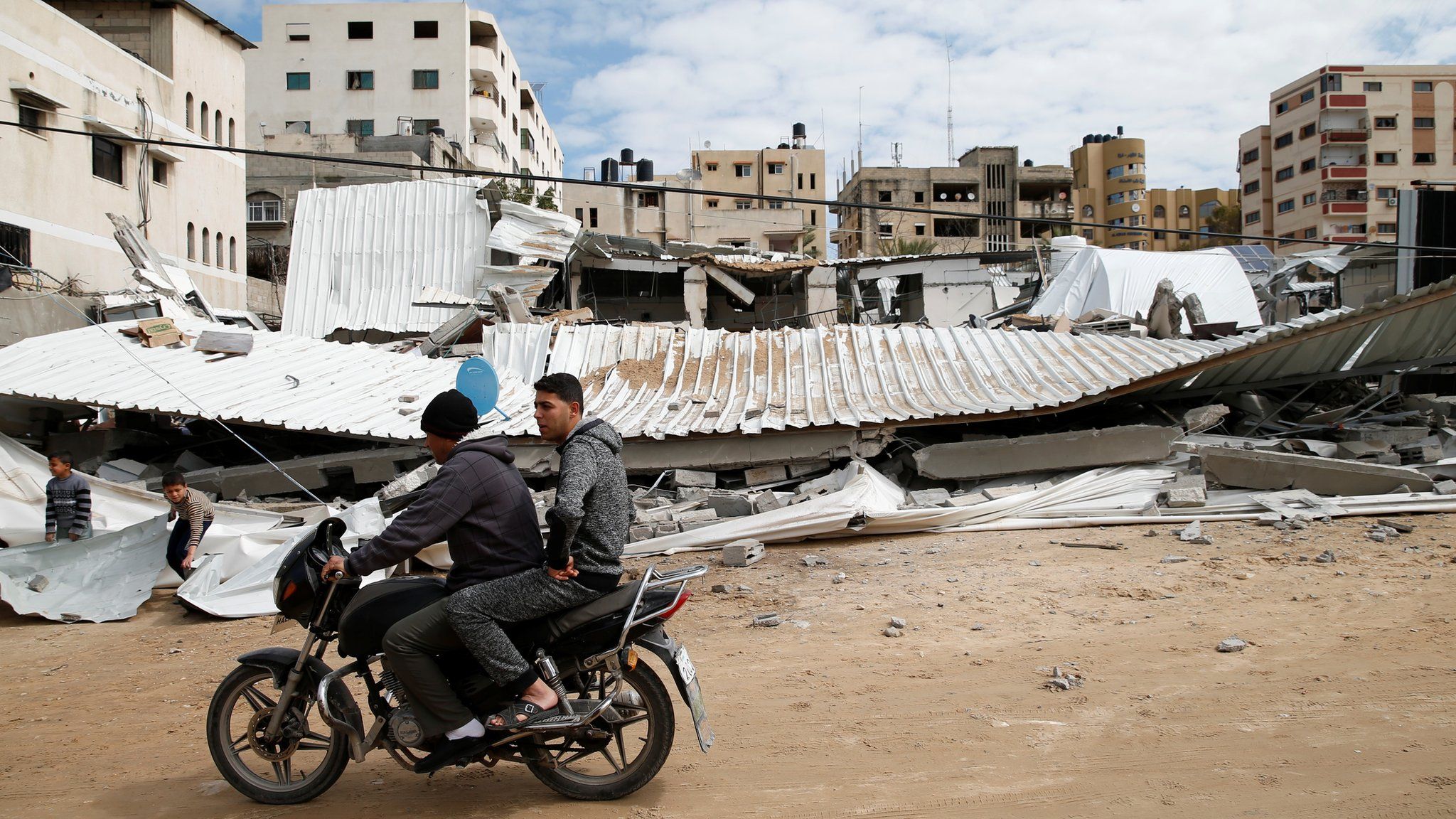 Palestinians drive past a Hamas site in Gaza City destroyed in an Israeli air strike (15 March 2019)
