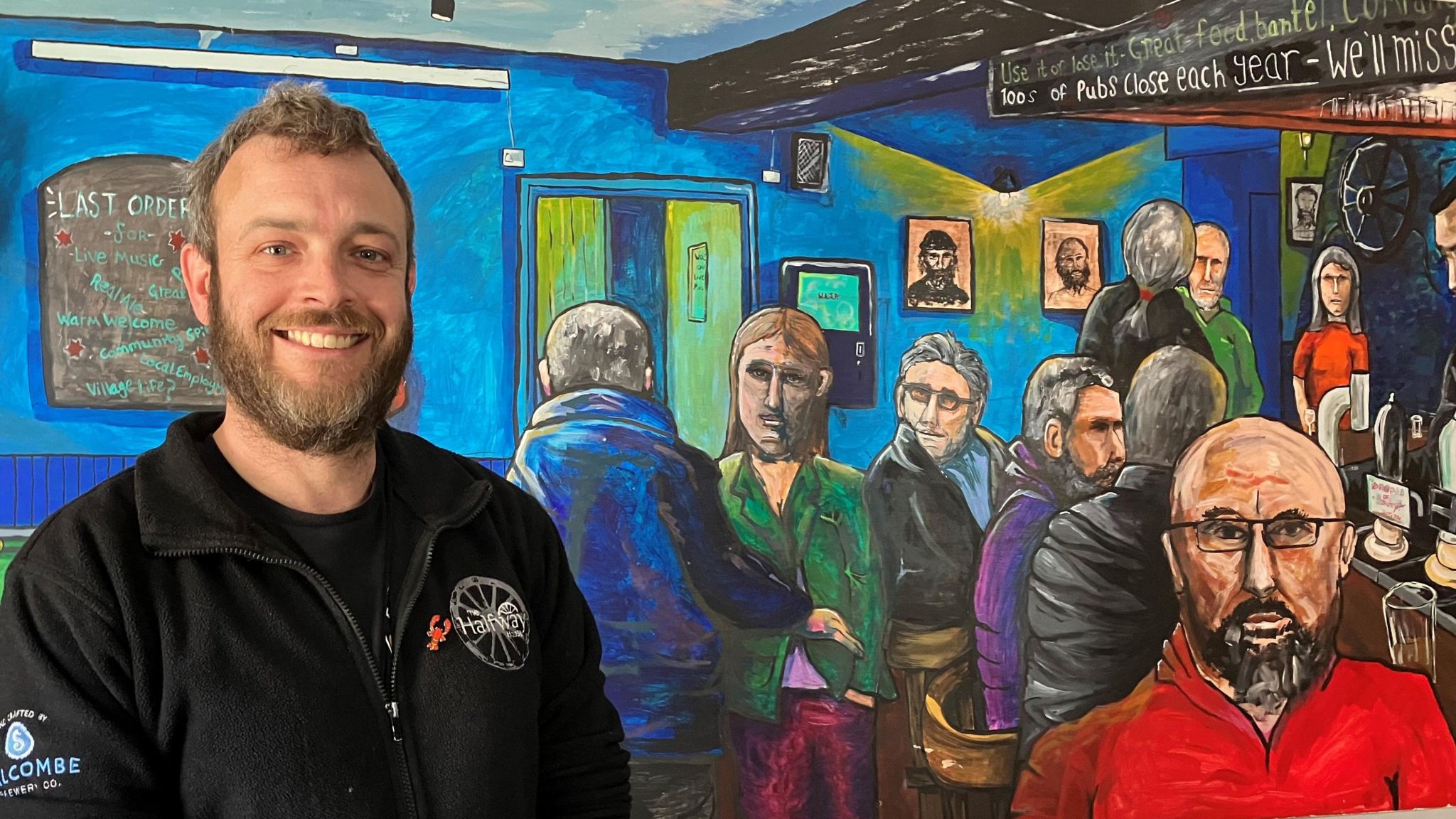 Man standing in pub in front of mural 