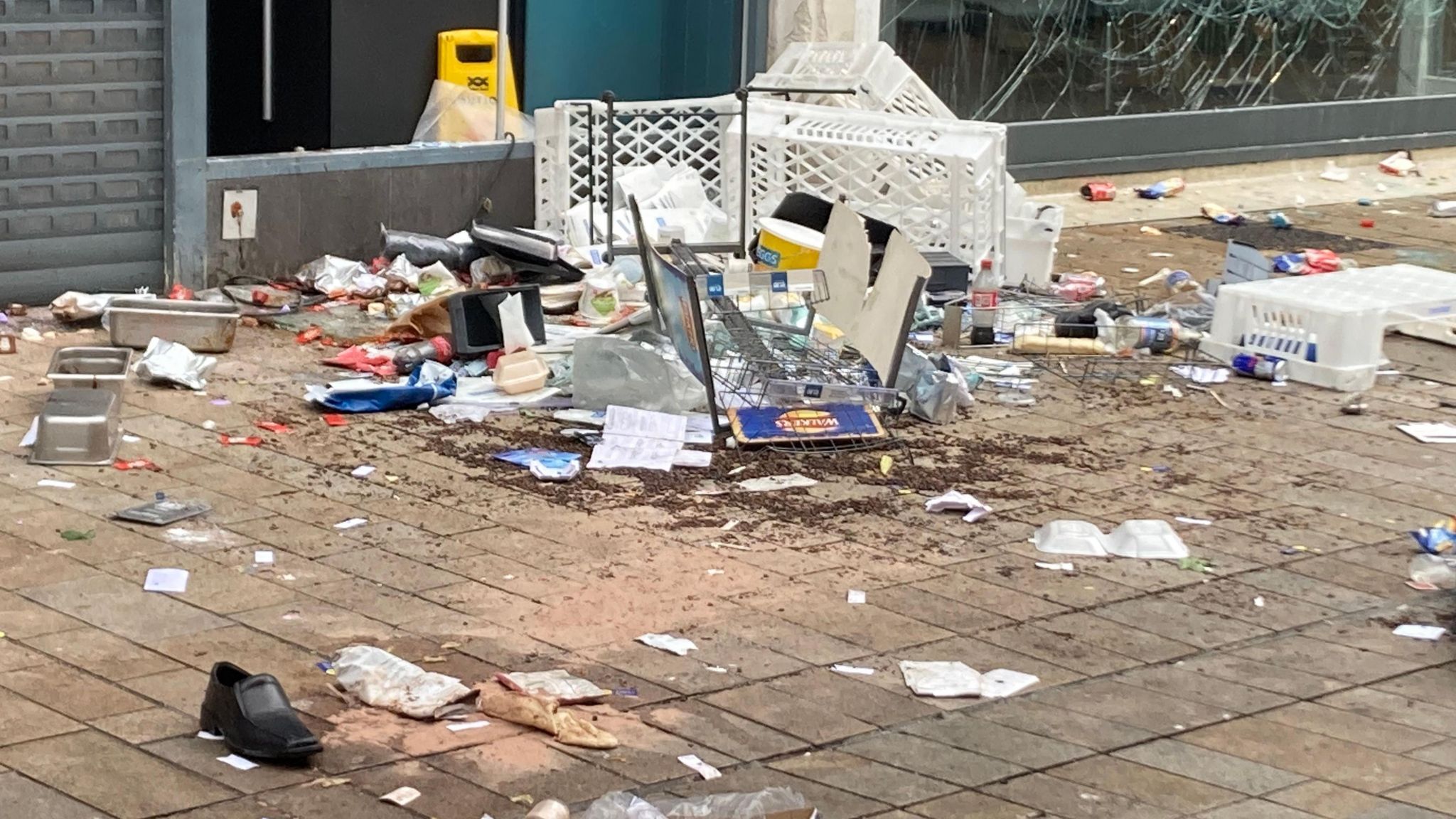 Baskets, a shoe, bottles and broken glass in a pile of rubbish on the street