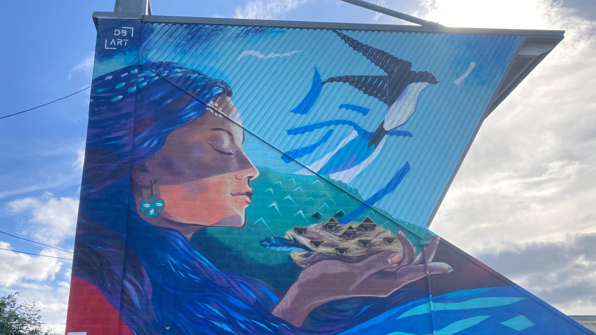 Mural of a woman wearing blue holding a nest of birds in her hand