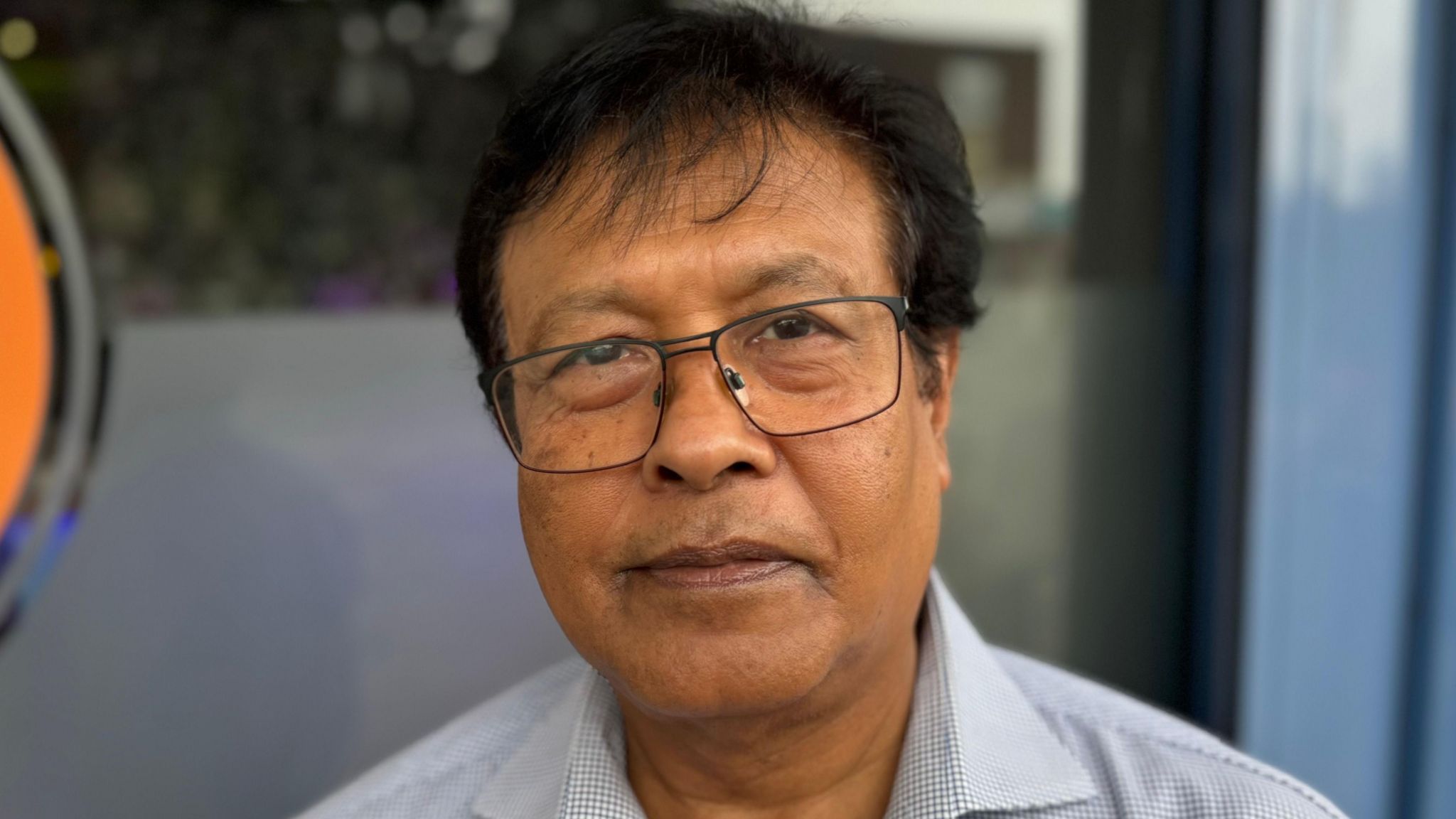 A man with dark hair and wearing glasses standing outside a restaurant