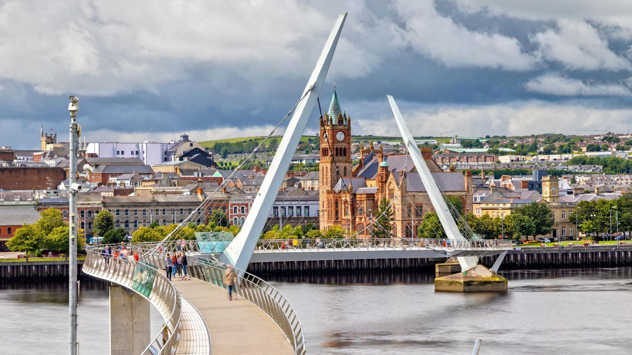 A view of Londonderry with the Peace Bridge over the Foyle river in the foreground and the Guildhall and other building in the background.