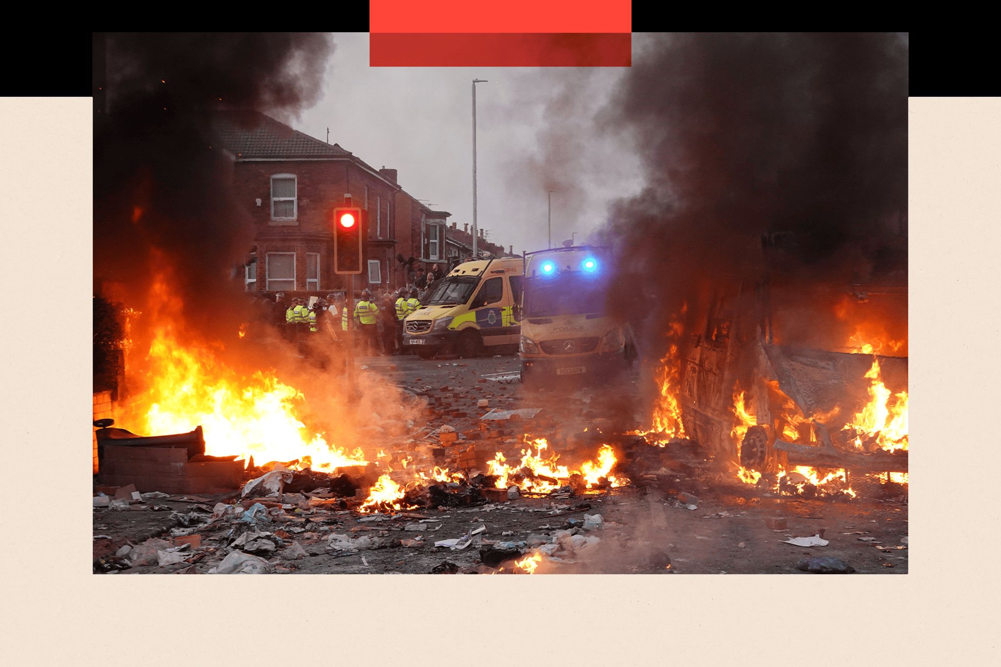 Colour image of riot police holding back protesters. In the foreground a police vehicle is engulfed by fire.