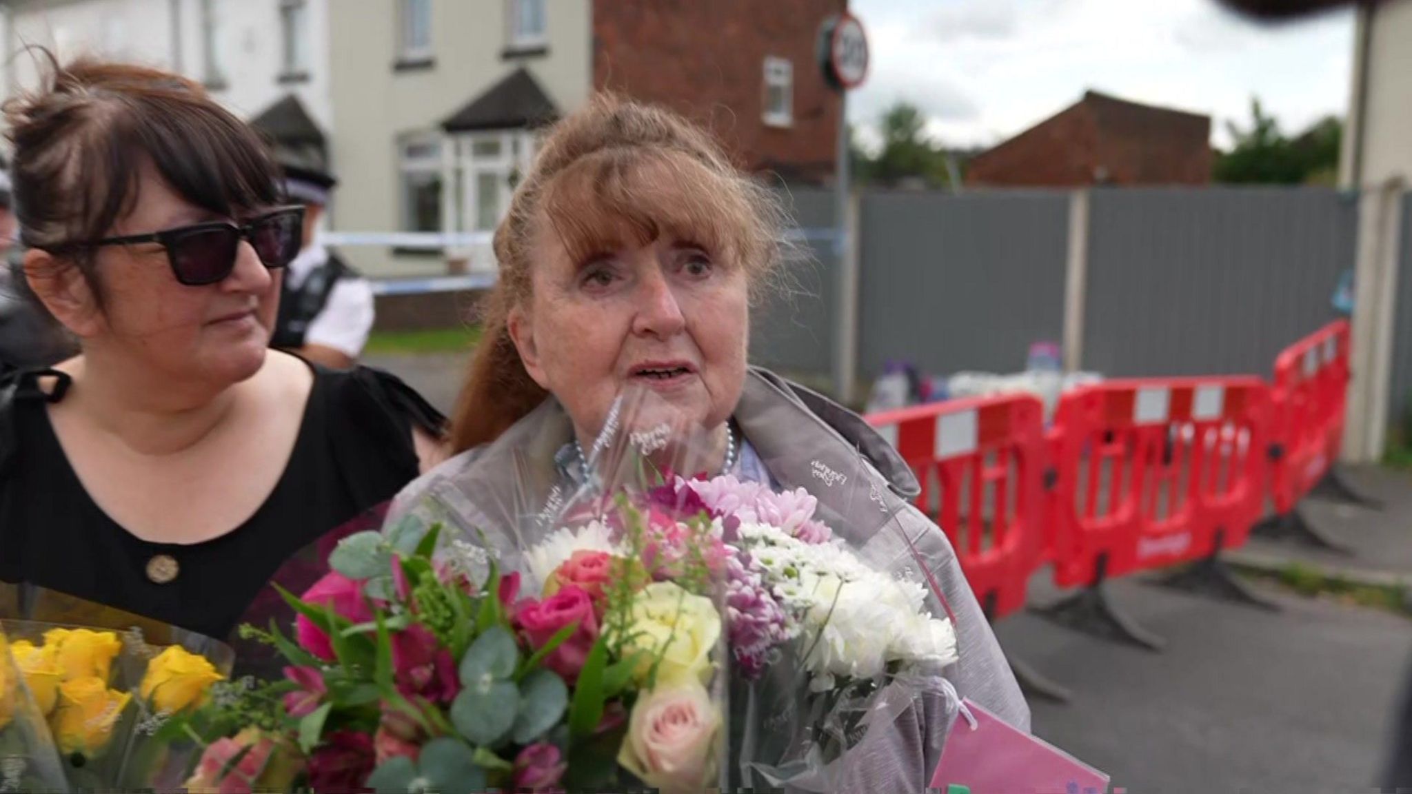 Elsie Dot Stancombe's aunt Jean Stevenson clutches a bouquet of flowers as she speaks to reporters close to the police cordon in Southport. She is comforted by a woman in dark glasses. 