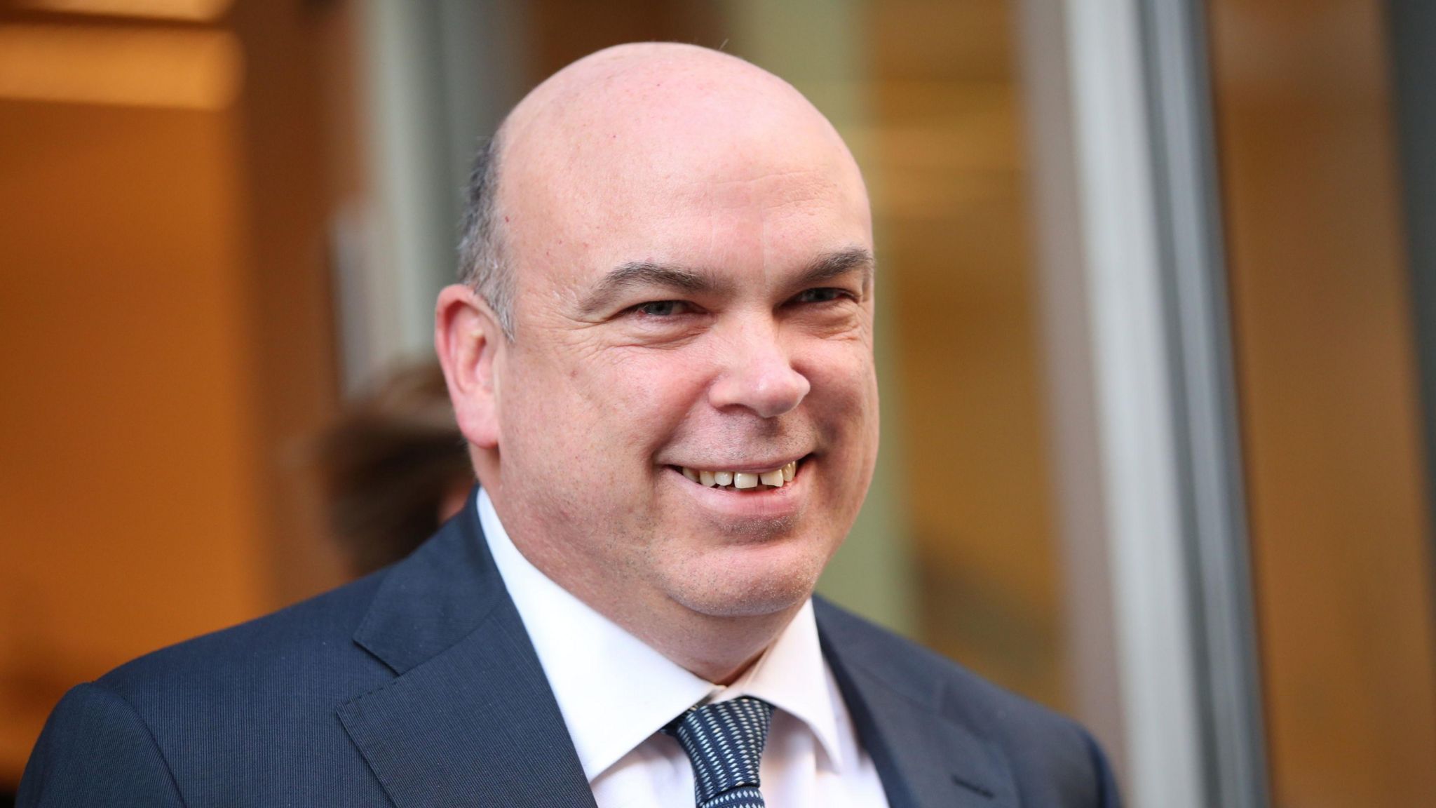 British technology tycoon Mike Lynch pictured from the shoulders up outside court in 2019. He is bald, smiling, and wearing a suit. 