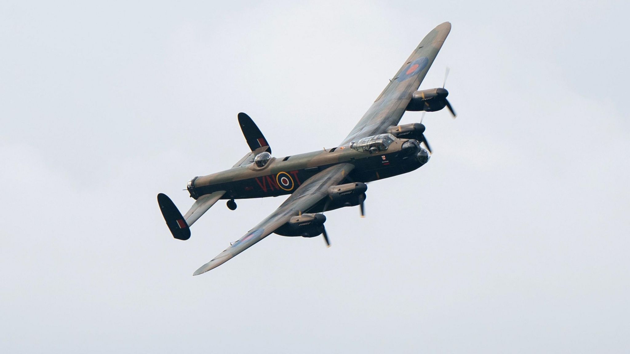 The PA474 Lancaster Bomber flying on an angle at an air show, with a cloudy sky in the background