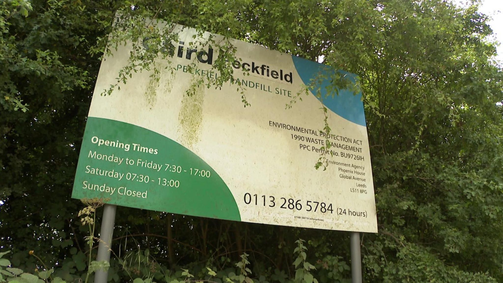 A sign outside the landfill site - it is white with green and blue graphics in opposite corners.