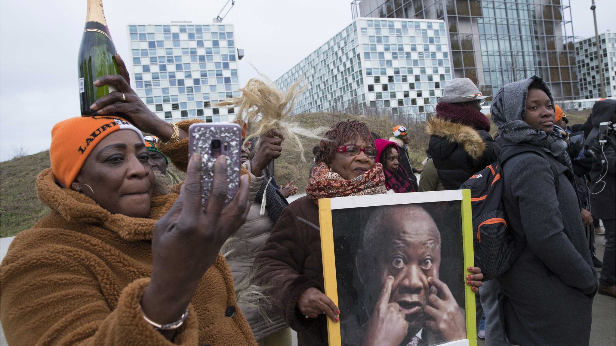 Supporters of Laurent Gbagbo rally outside the ICC, holding up a photo of him and a bottle of champagne