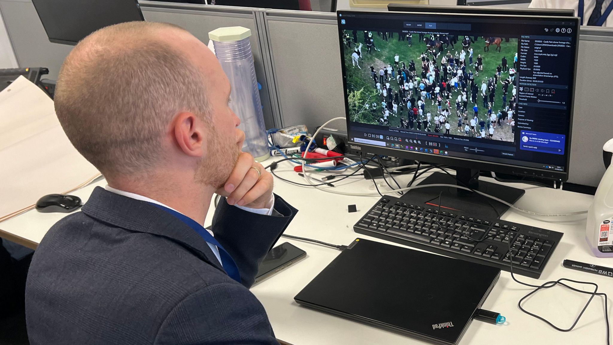 A man wearing in a suit scrolling through footage on his computer at a desk