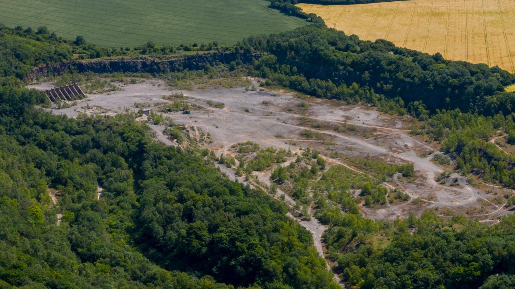 An aerial image of Westdown Quarry. It is a large dug out space surrounded by green fields and thick woodland