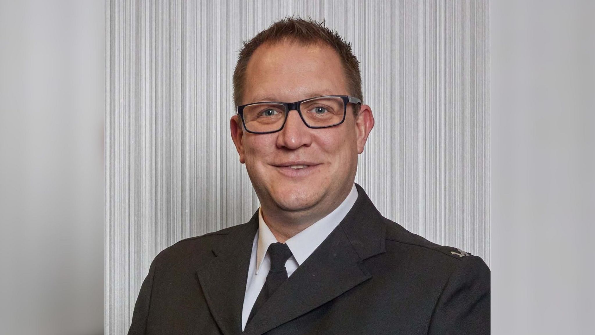 PC Tom Scott has short, dark hair and is wearing thick rimmed, rectangular glasses. He is wearing a formal police uniform and is smiling for the camera.