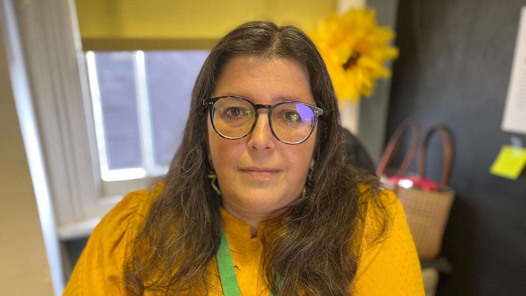 A woman with long brown hair sitting in an office wearing a yellow top in front of a sunflower