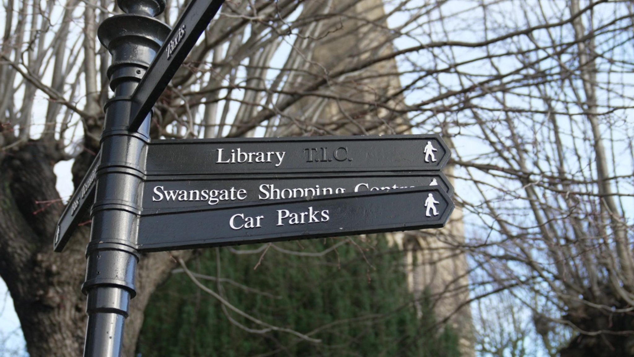 A black sign in Wellingborough pointing pedestrians to locations including the library, Swansgate shopping centre and car parks 