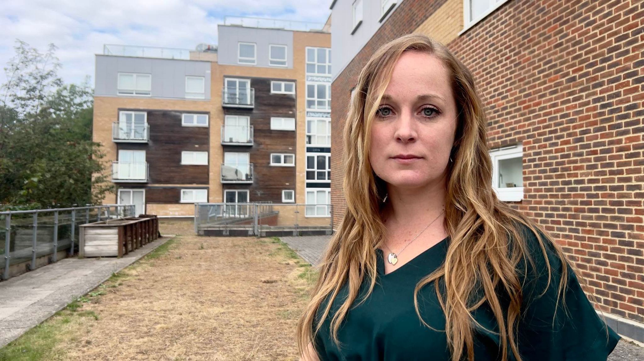 Jennifer Viccars standing in front of the block of flats. She is wearing a green T-shirt.