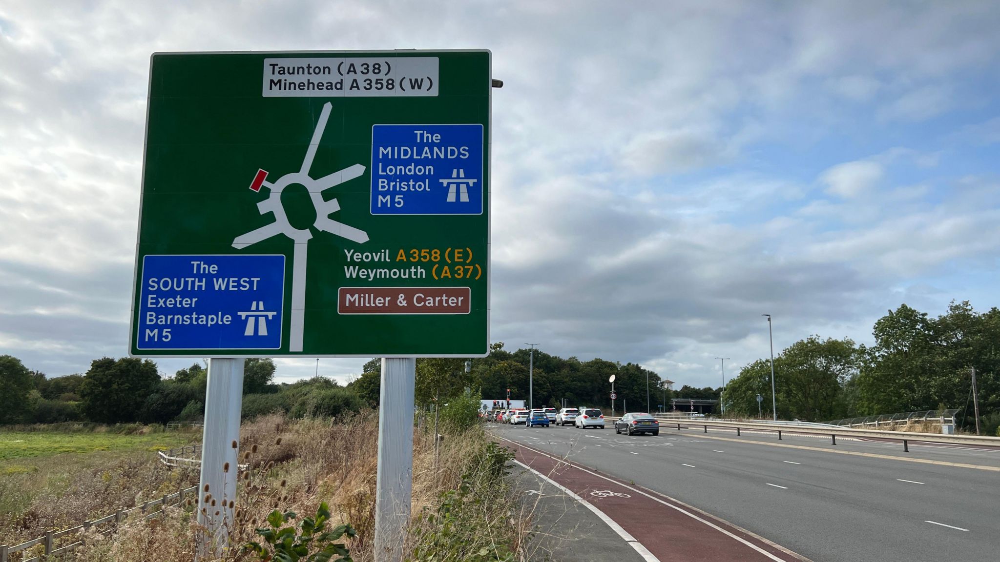 Roundabout sign showing the M5 and A358 roads with a roundabout in the background