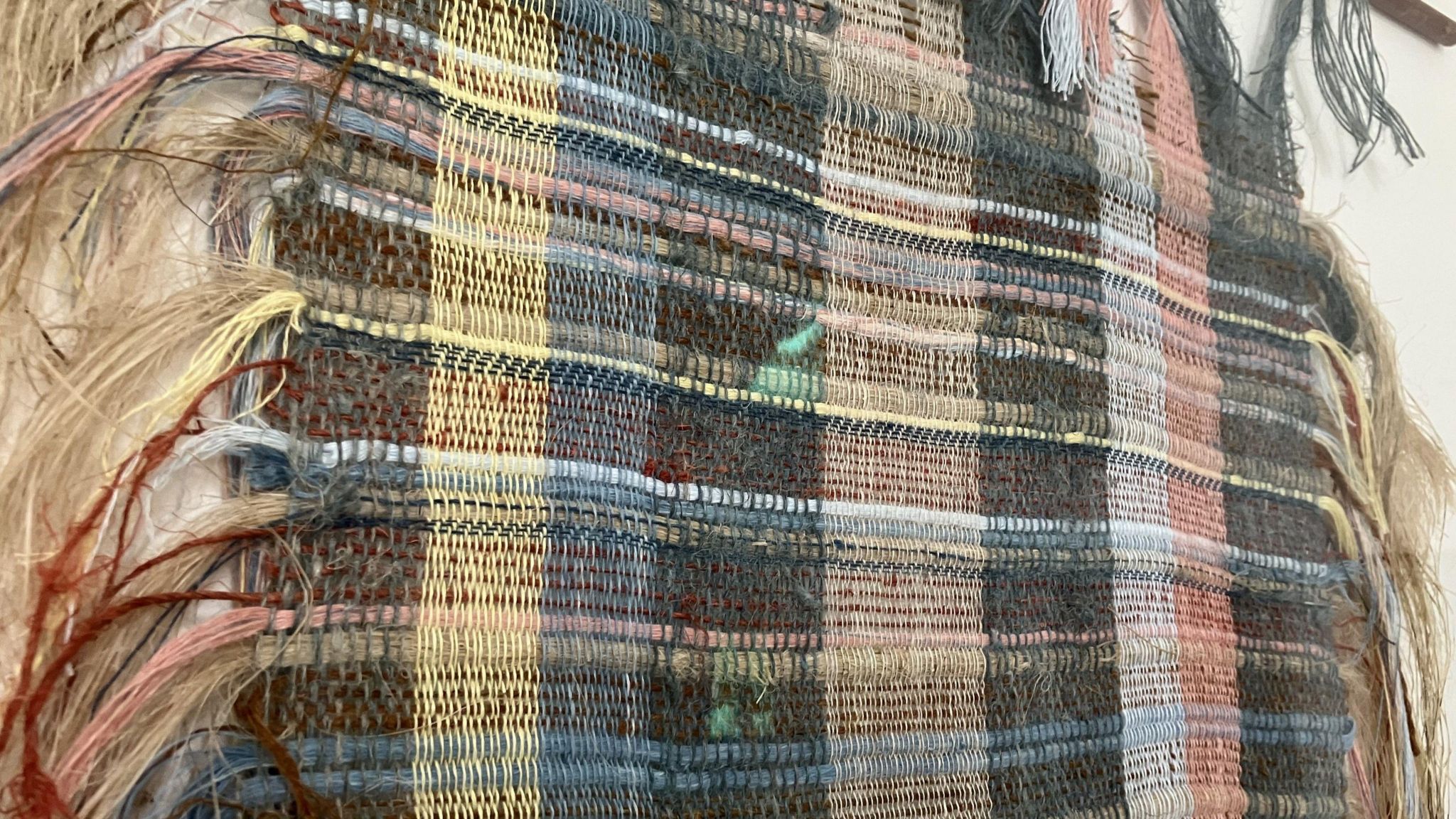 A colourful fabric made from hemp fibres is displayed on a white wall