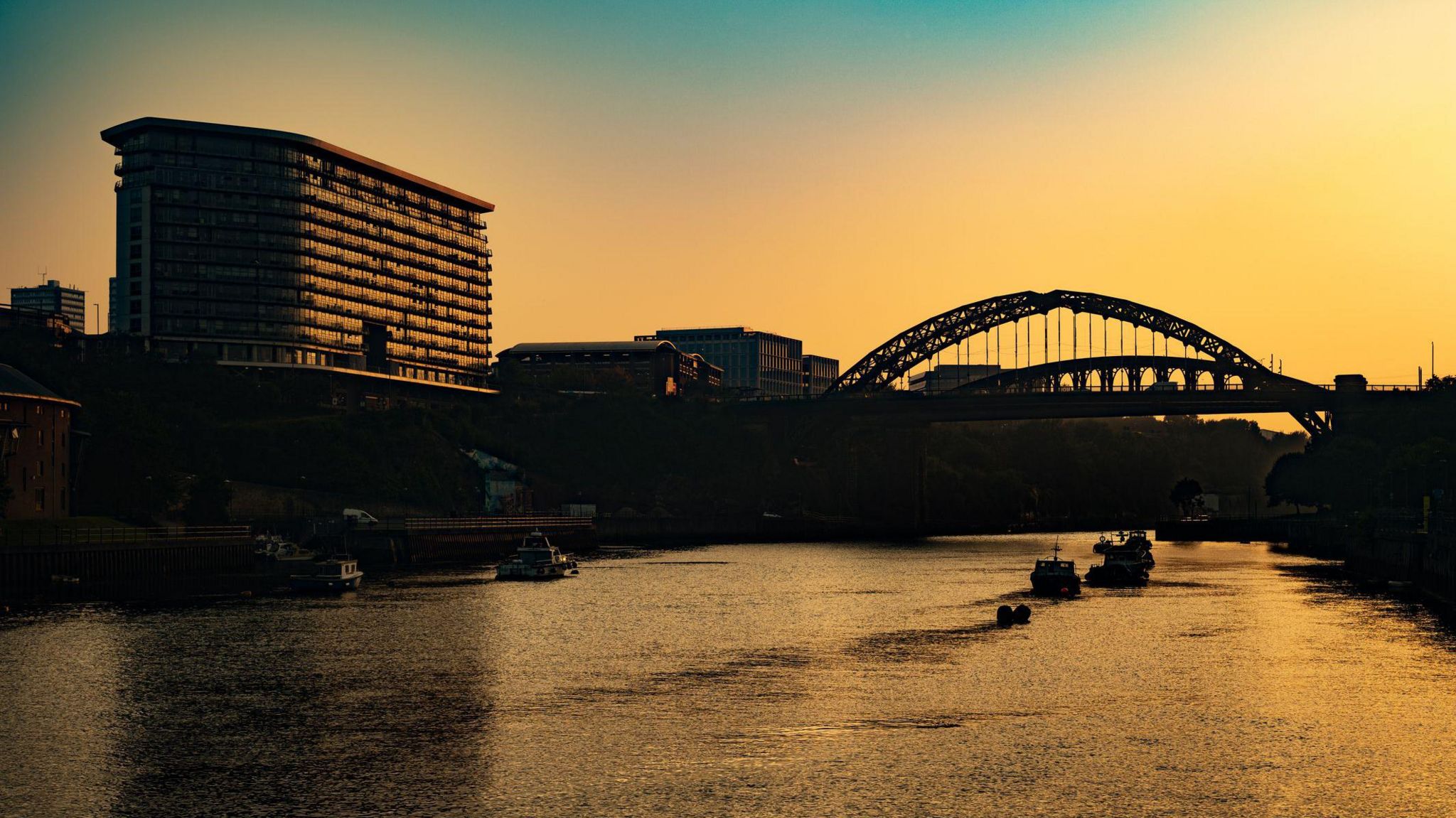 A building and bridge silhouetted against a yellow sunrise