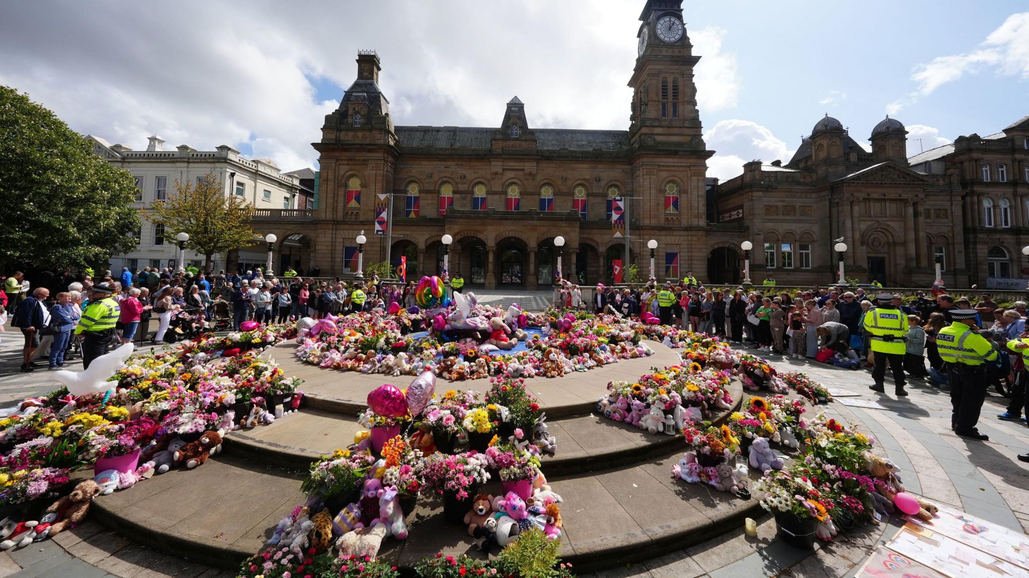 Flowers and balloons sit in the centre on ground, outside a theatre