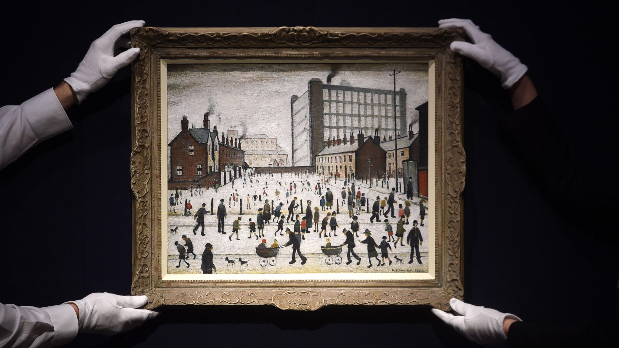 Two people in white gloves hold LS Lowry's artwork, The Mill, Pendlebury, which depicts a crowd of people in front of terraced houses and a mill