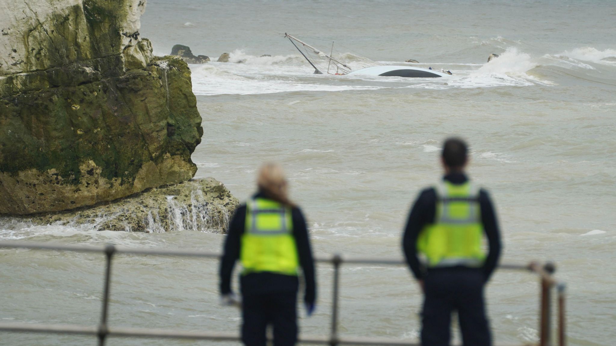 Two Border Force officers look at the capsized yacht near Seaford