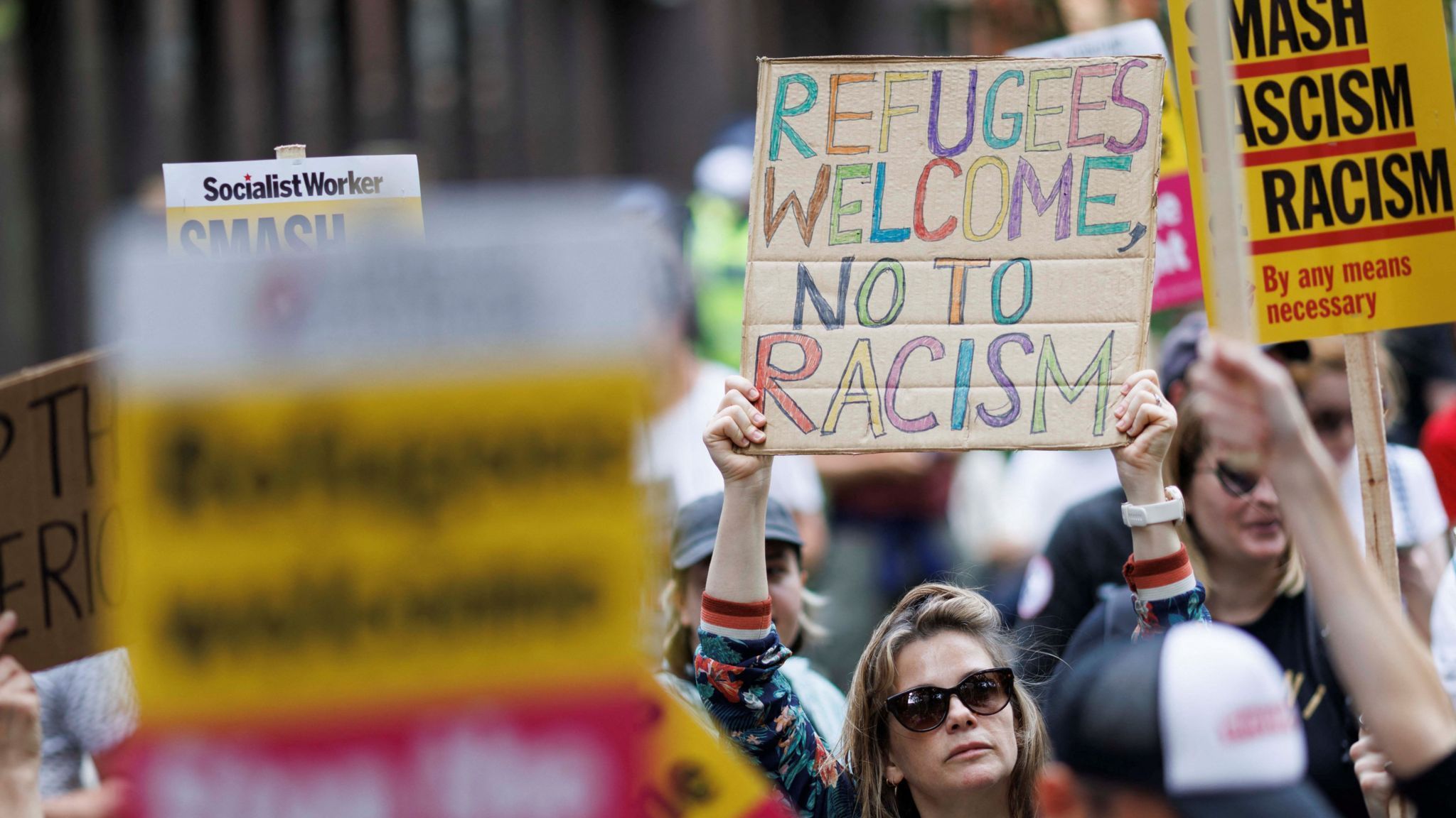 A woman holds a sign welcoming refugees and condemning racism