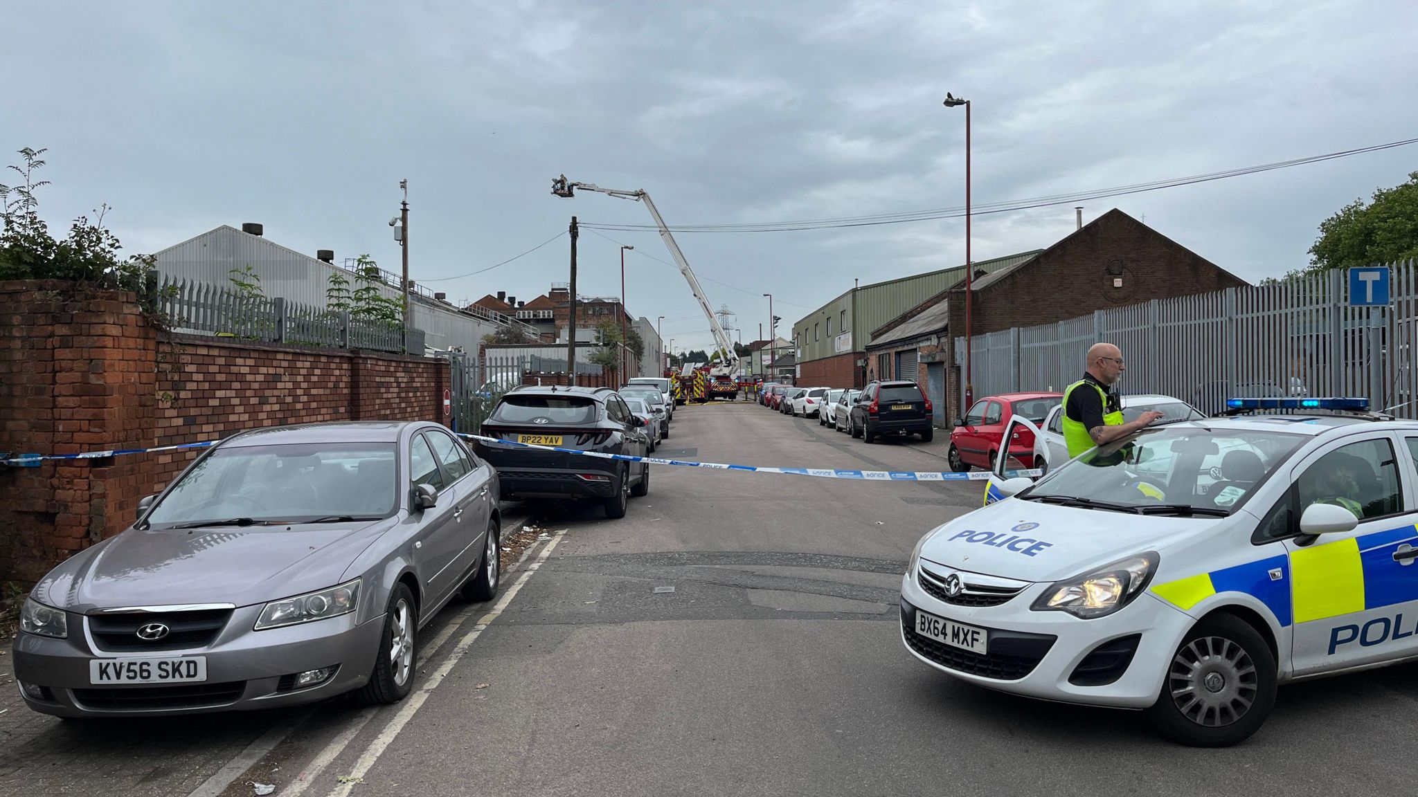 A police cordon on a street, and a fire engine using its aerial platform in the background