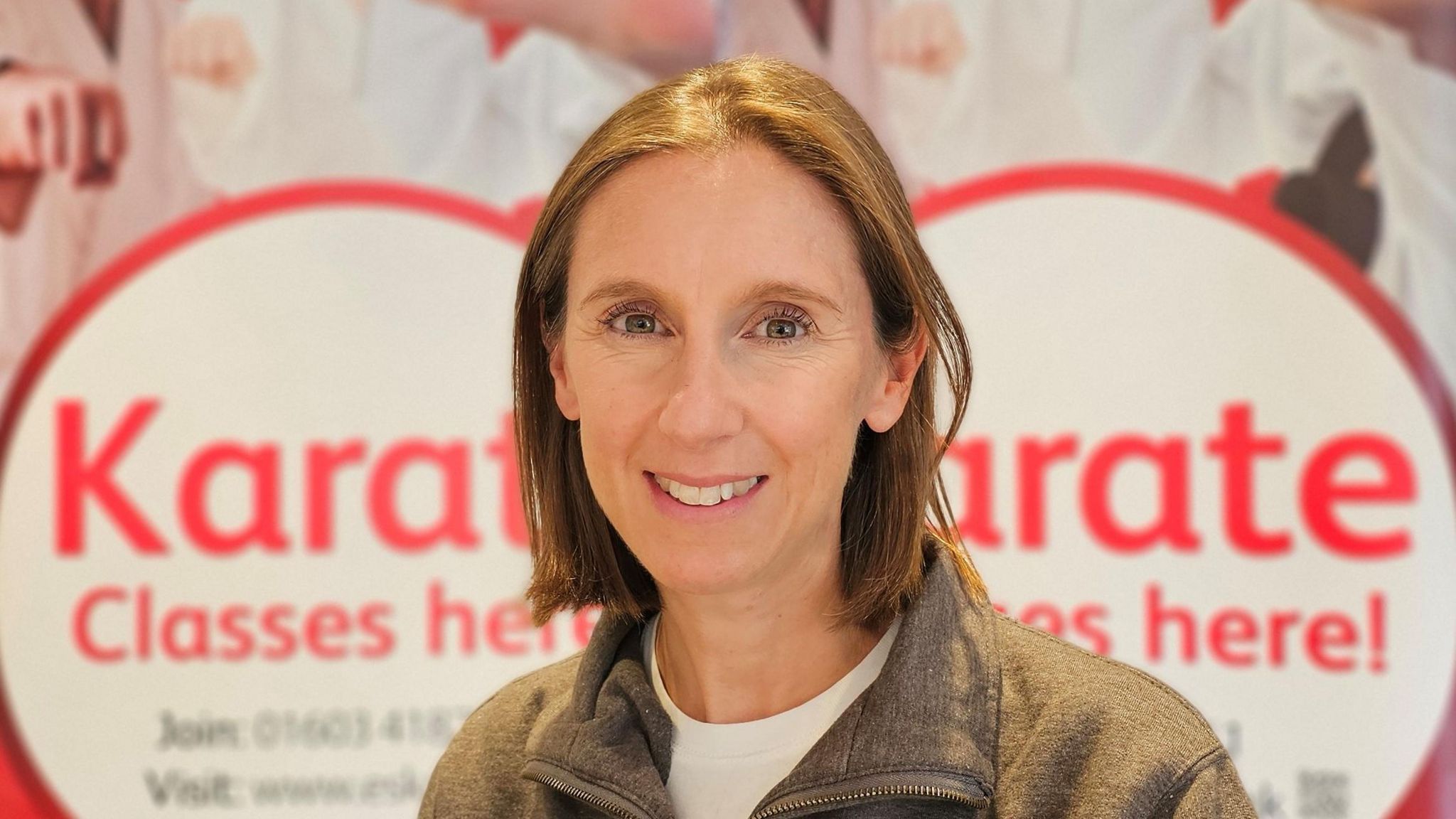 Eve Dewsnap smiling in front of a board advertising karate classes