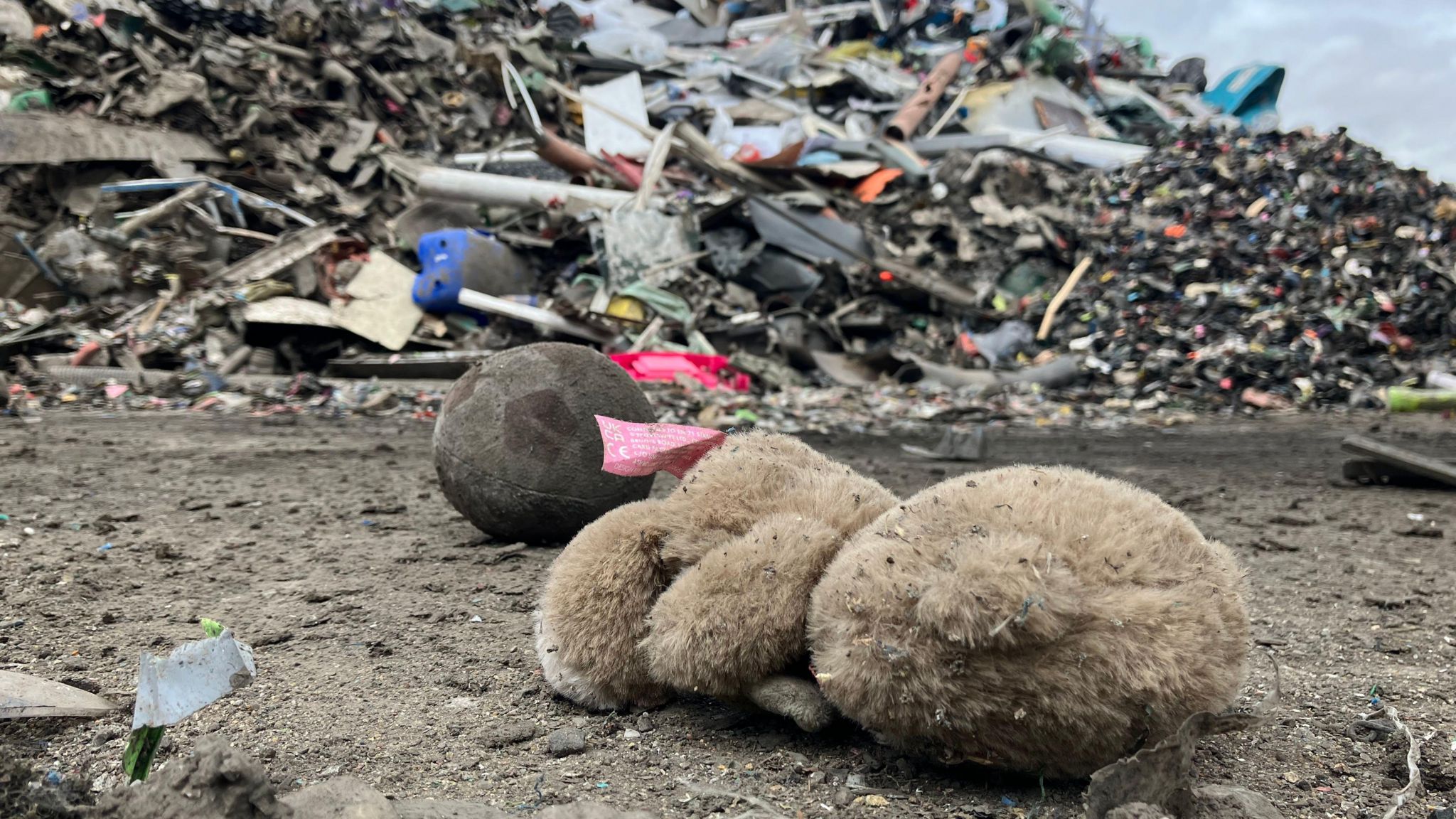 A soft toy and ball lying in front of a large pile of rubbish