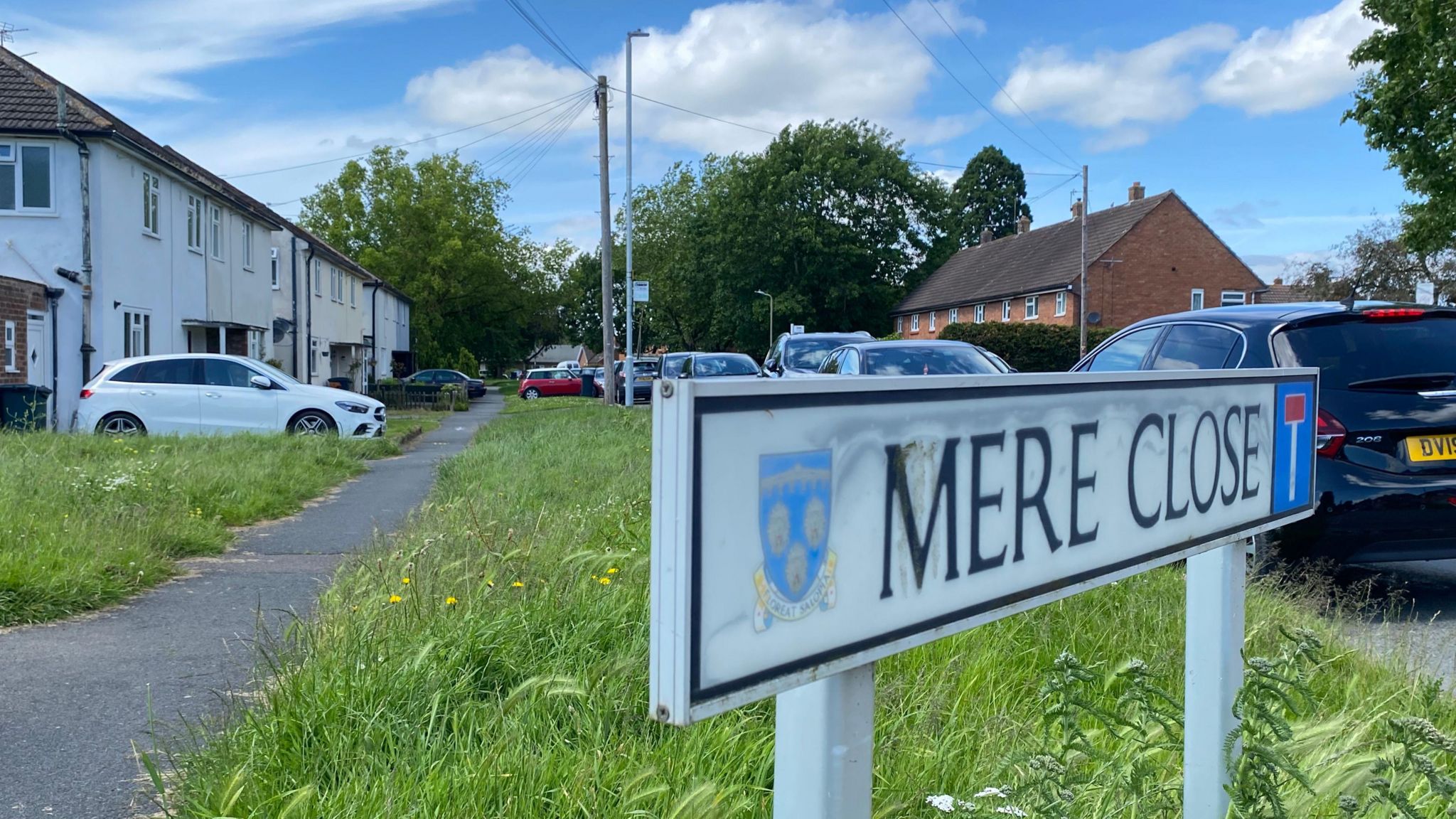 A street sign for Mere Close, with cars parked along the road in the background