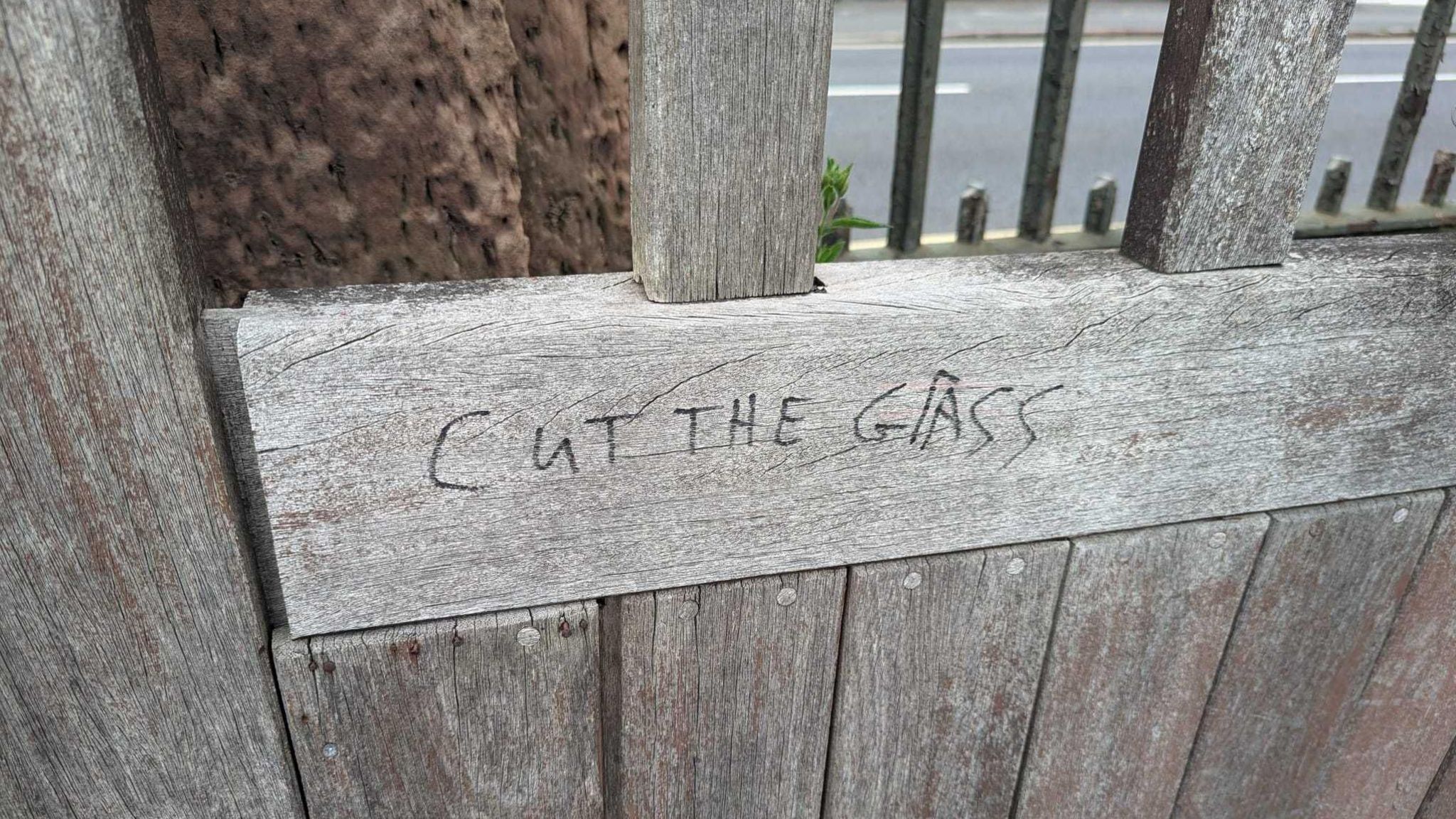 Graffiti saying cut the grass written on a wooden gate