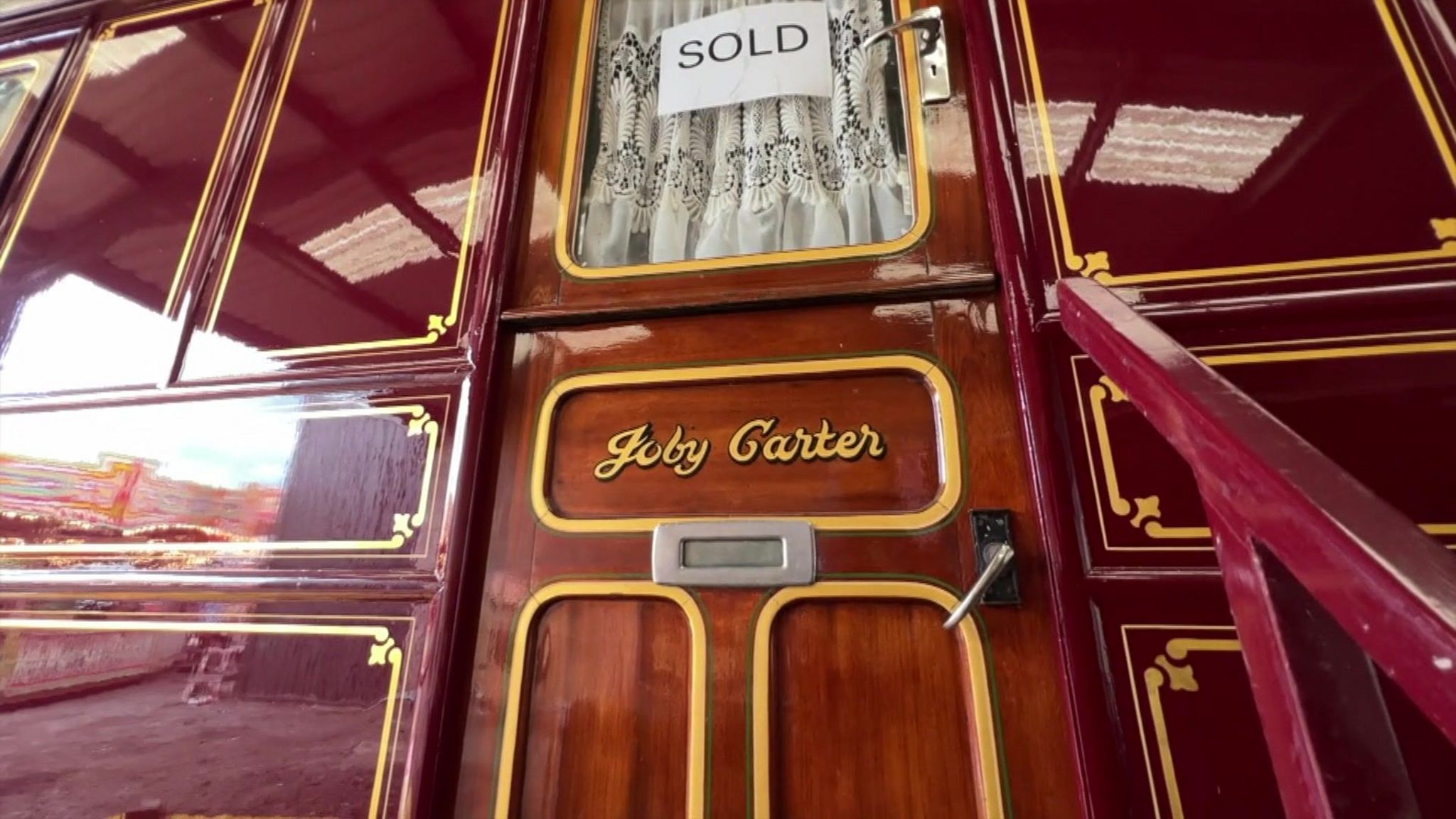 The door of a red painted caravan bearing the name Joby Carter and a white sold sign